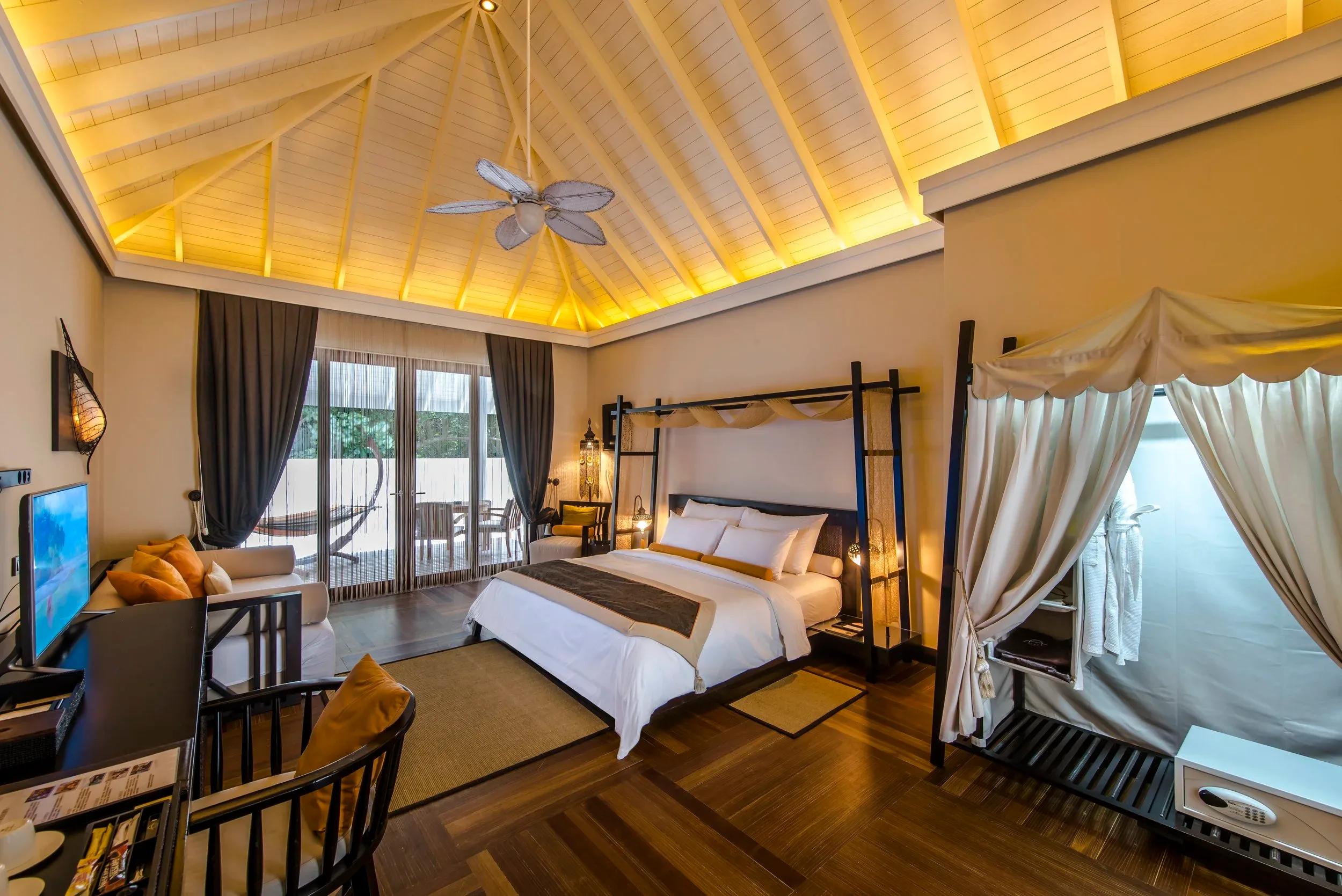A Garden Villa bedroom under a vaulted thatch ceiling, glass doors opening onto a private garden with a hammock