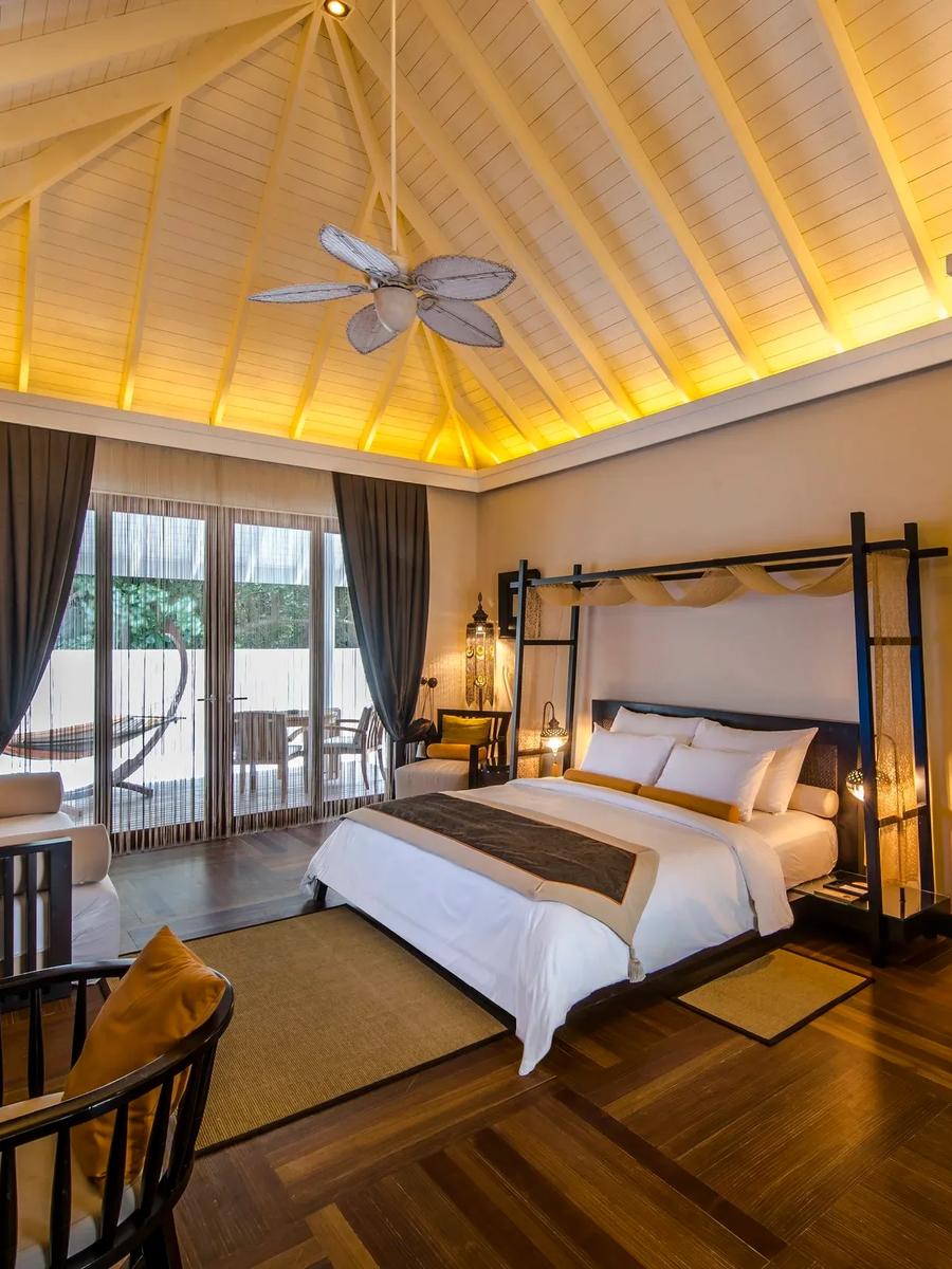 A Garden Villa bedroom under a vaulted thatch ceiling, glass doors opening onto a private garden with a hammock