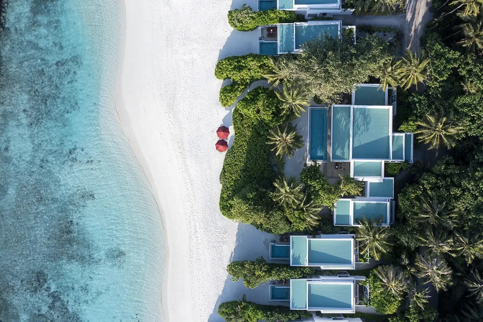 Top-down aerial of Niva Dhigali's beachfront villas and jungle, white sand meeting the reef edge