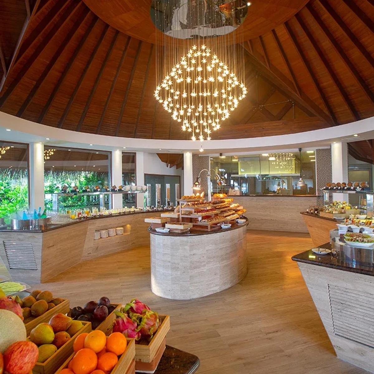 Lime Restaurant's breakfast buffet spread beneath a star-shaped chandelier, fresh fruit in the foreground and the open kitchen behind
