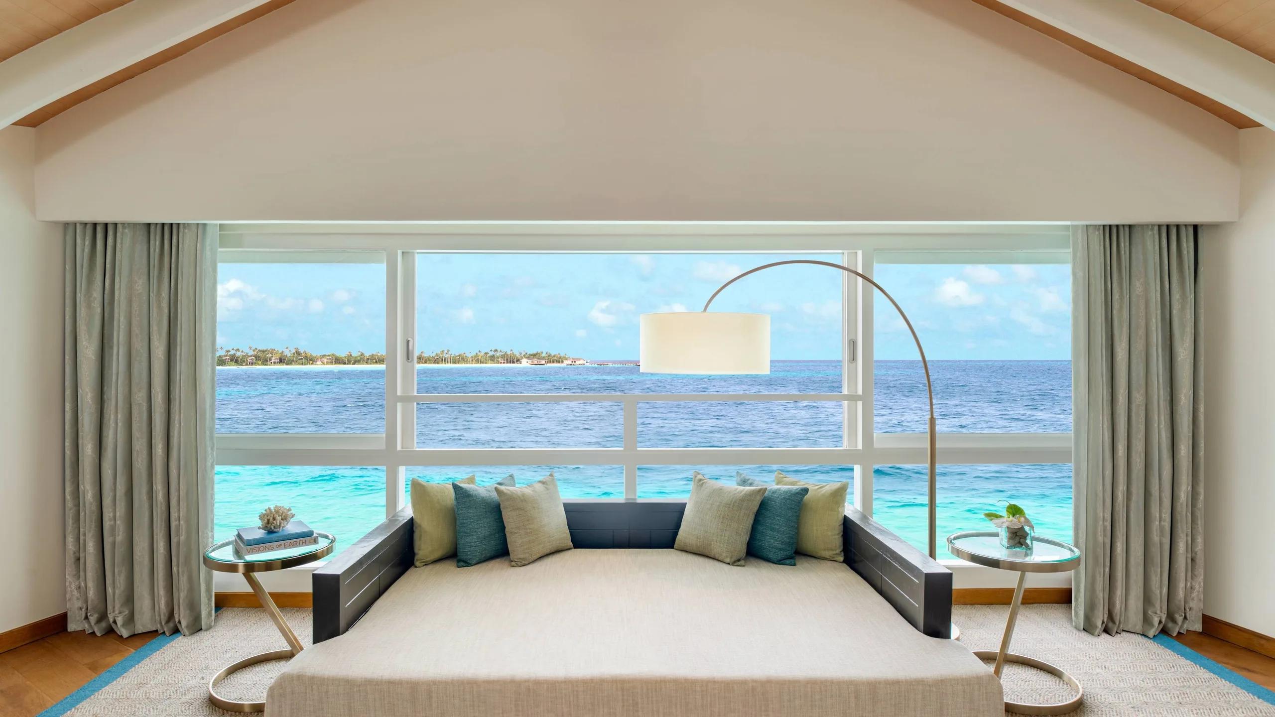 The upstairs lounge of the Duplex Overwater Pool Villa, a built-in daybed facing floor-to-ceiling windows over open water
