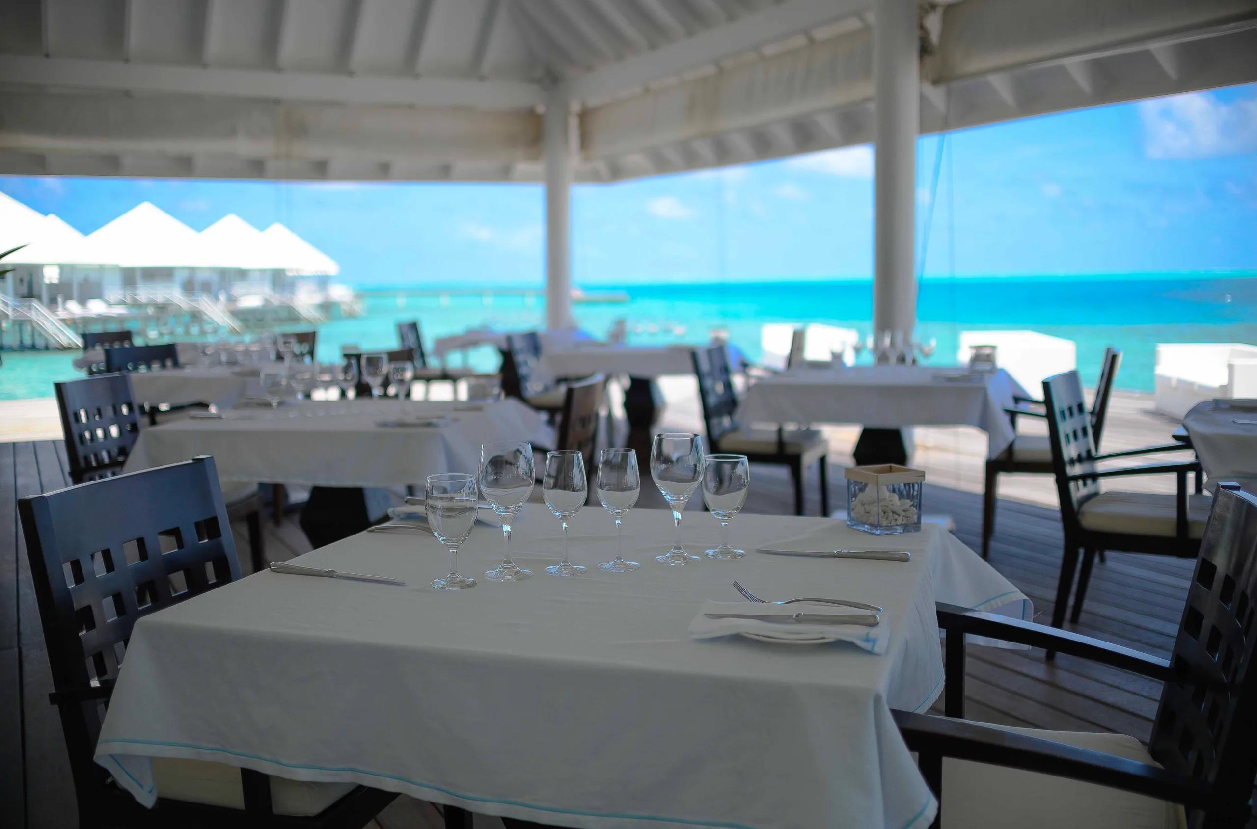 Tables set for dinner at Aqua Over Water Restaurant, overwater villas visible across the lagoon