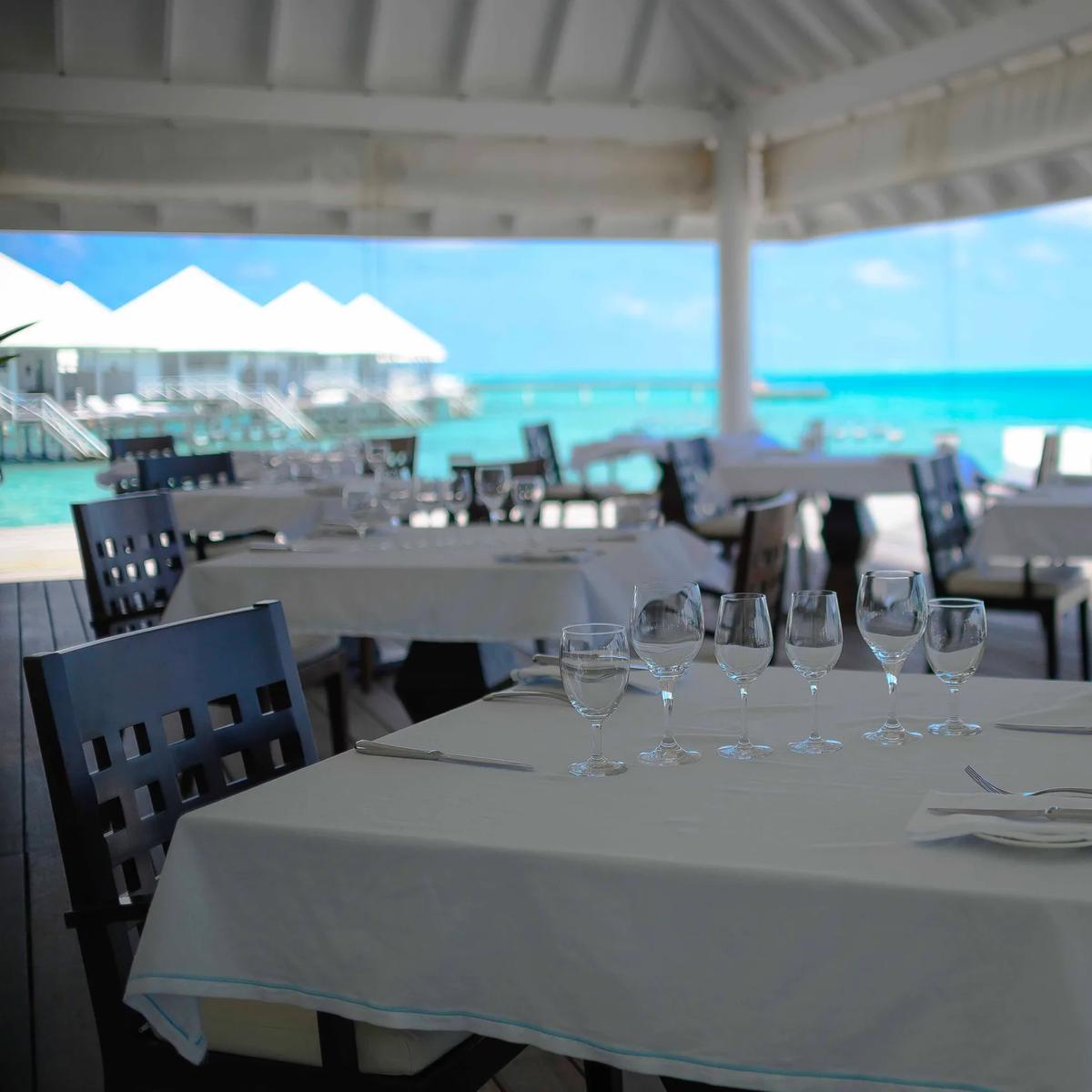 Tables set for dinner at Aqua Over Water Restaurant, overwater villas visible across the lagoon