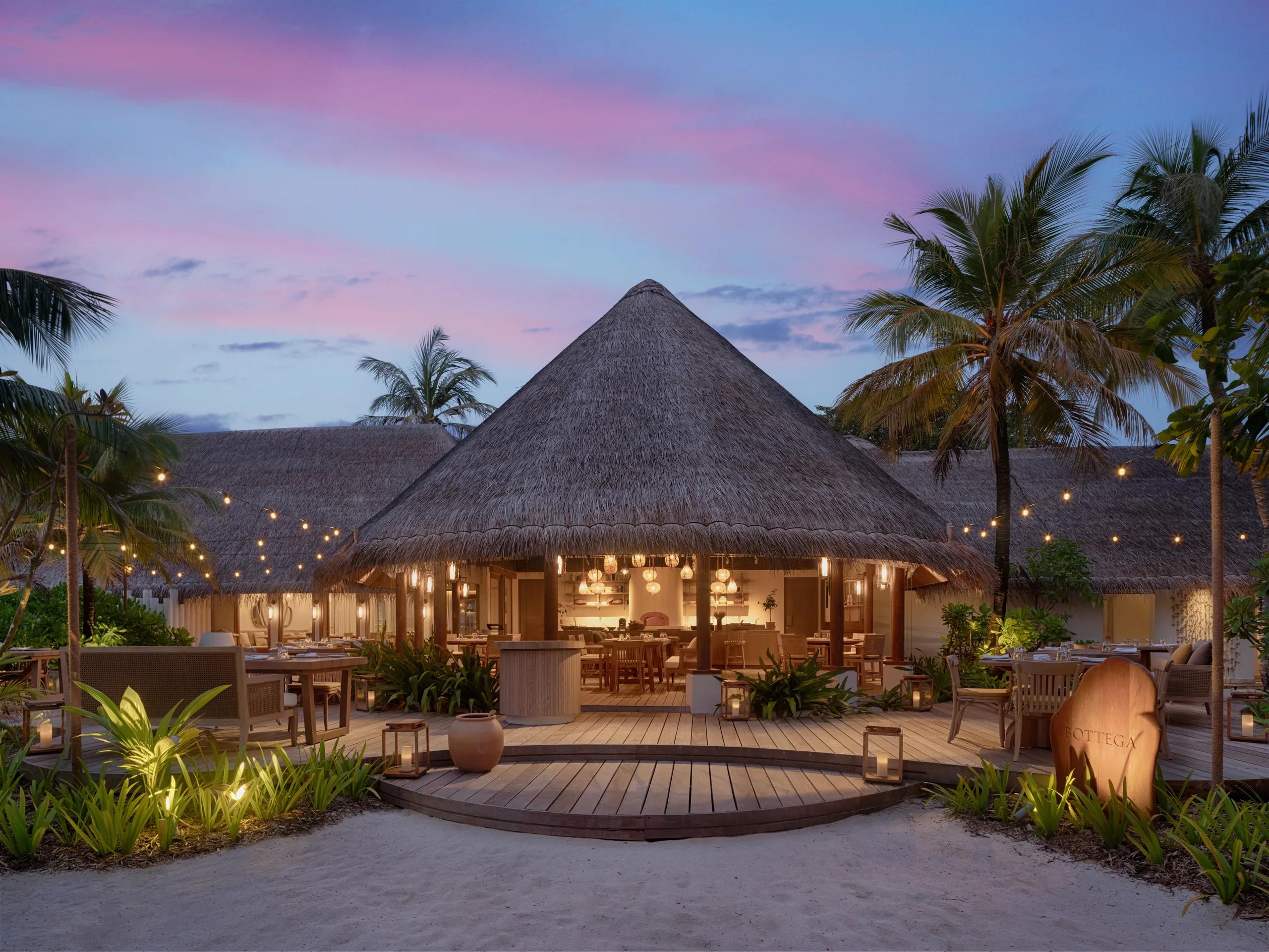 Bottega's thatched-roof dining pavilion lit for dinner, with outdoor tables and string lights at dusk.