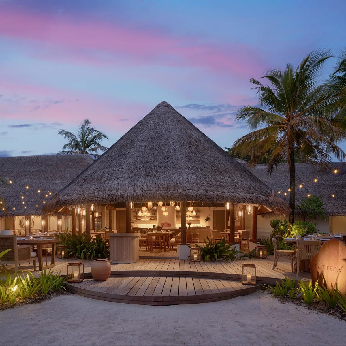 Bottega's thatched-roof dining pavilion lit for dinner, with outdoor tables and string lights at dusk.