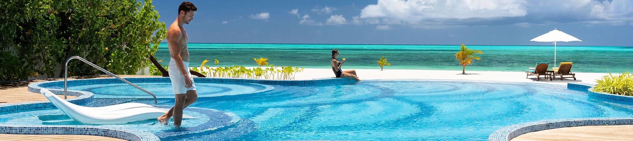 A resort pool deck merging into the beach and lagoon beyond