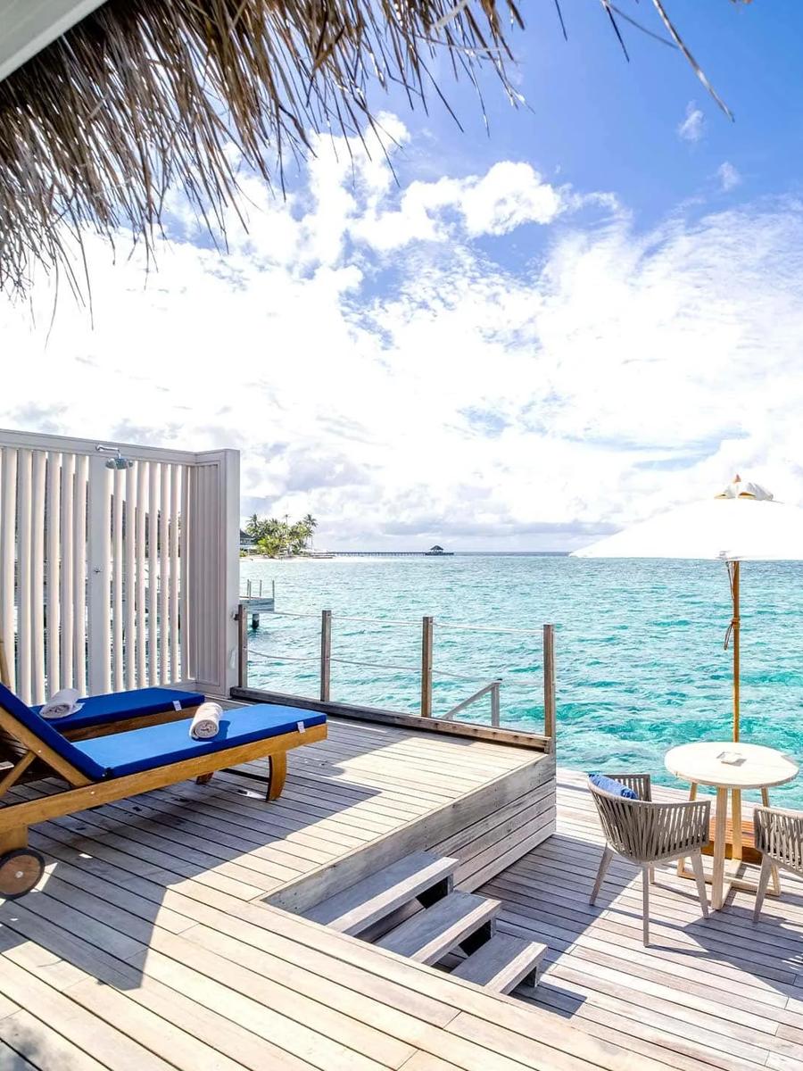 Sun loungers and a table for two on a Water Villa's overwater deck at Baglioni Maldives, with a neighbouring island on the horizon