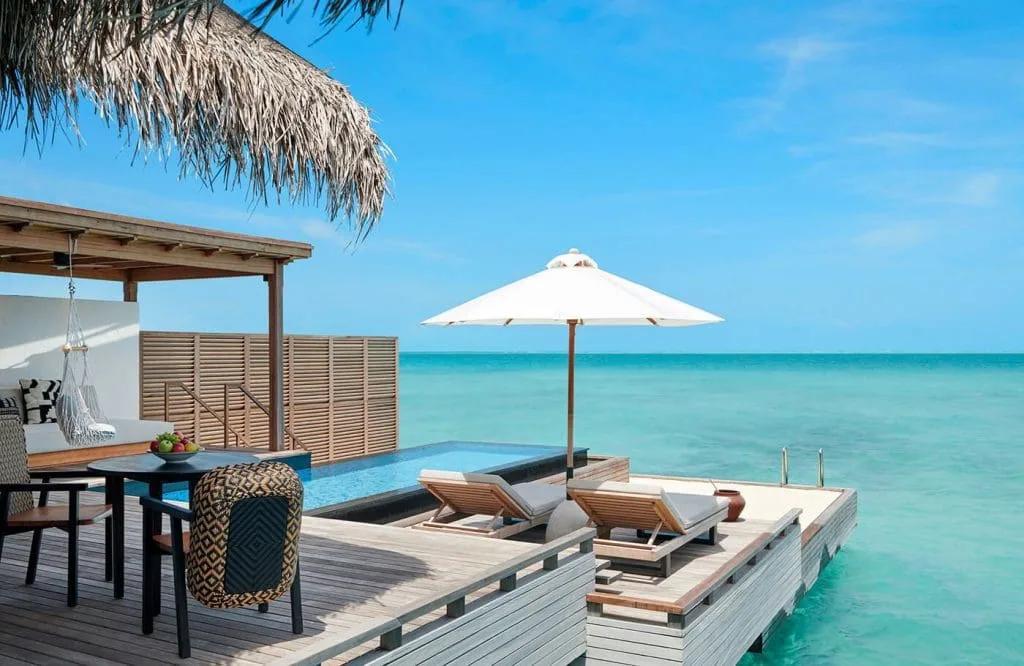Overwater deck with a private pool, a shaded daybed with a hanging chair, and open lagoon views