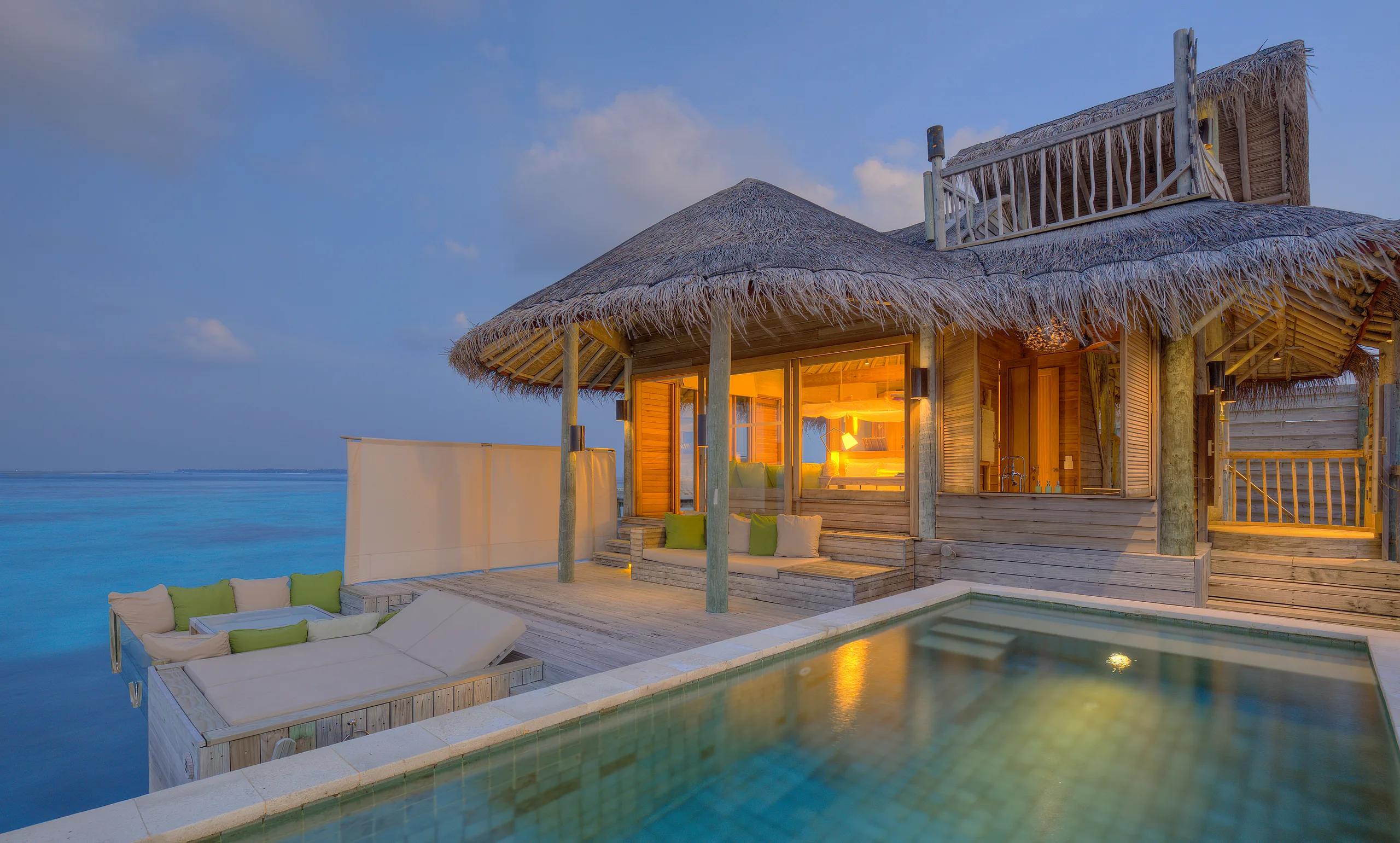 An Ocean Water Villa with Pool lit up at dusk, its private pool and deck extending over the lagoon