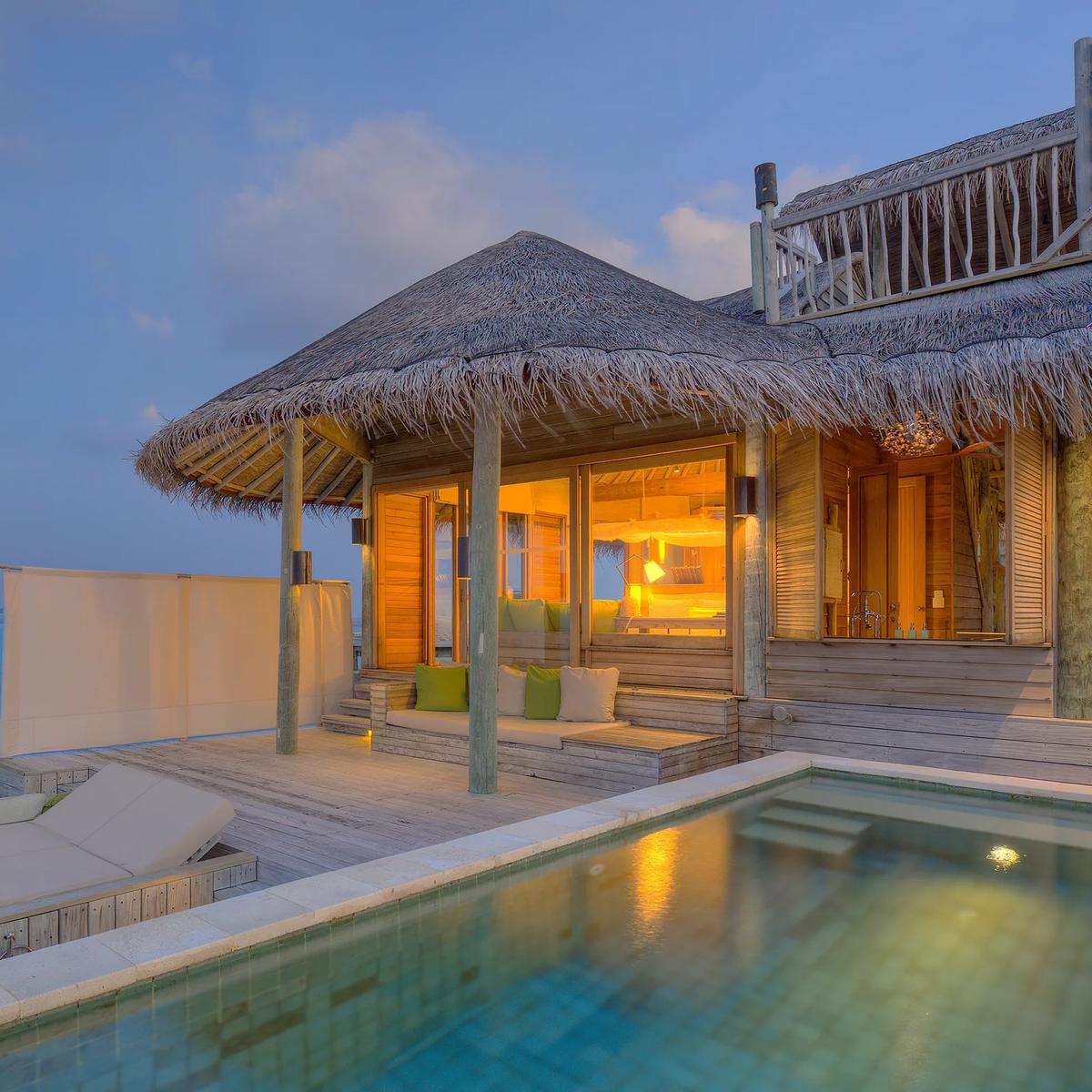 A villa pool deck lit up at dusk with a lounge area beside it, the setting for in-villa dining