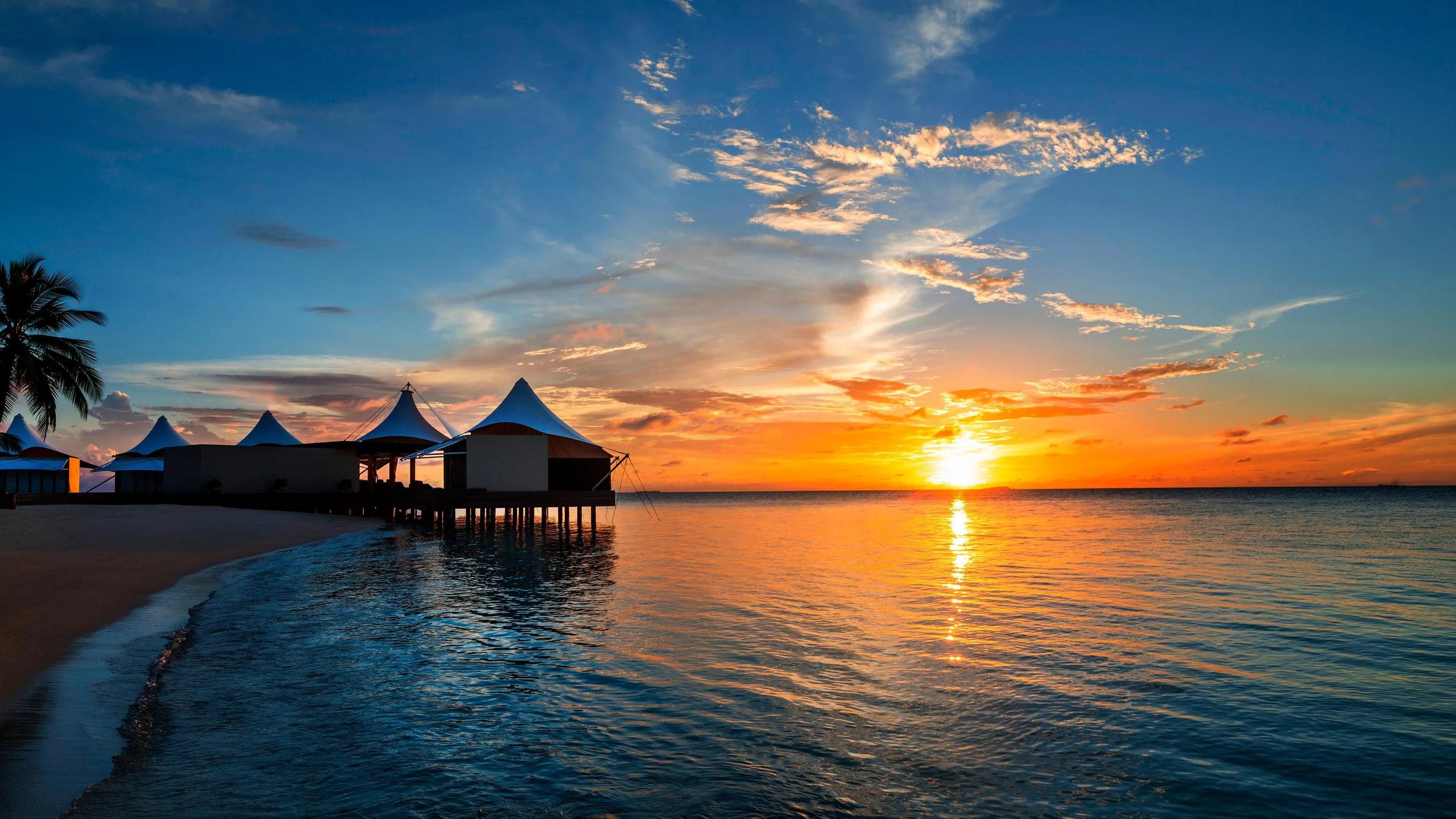 AWAY Spa's sail-shaped overwater pavilions at W Maldives, silhouetted against the sunset