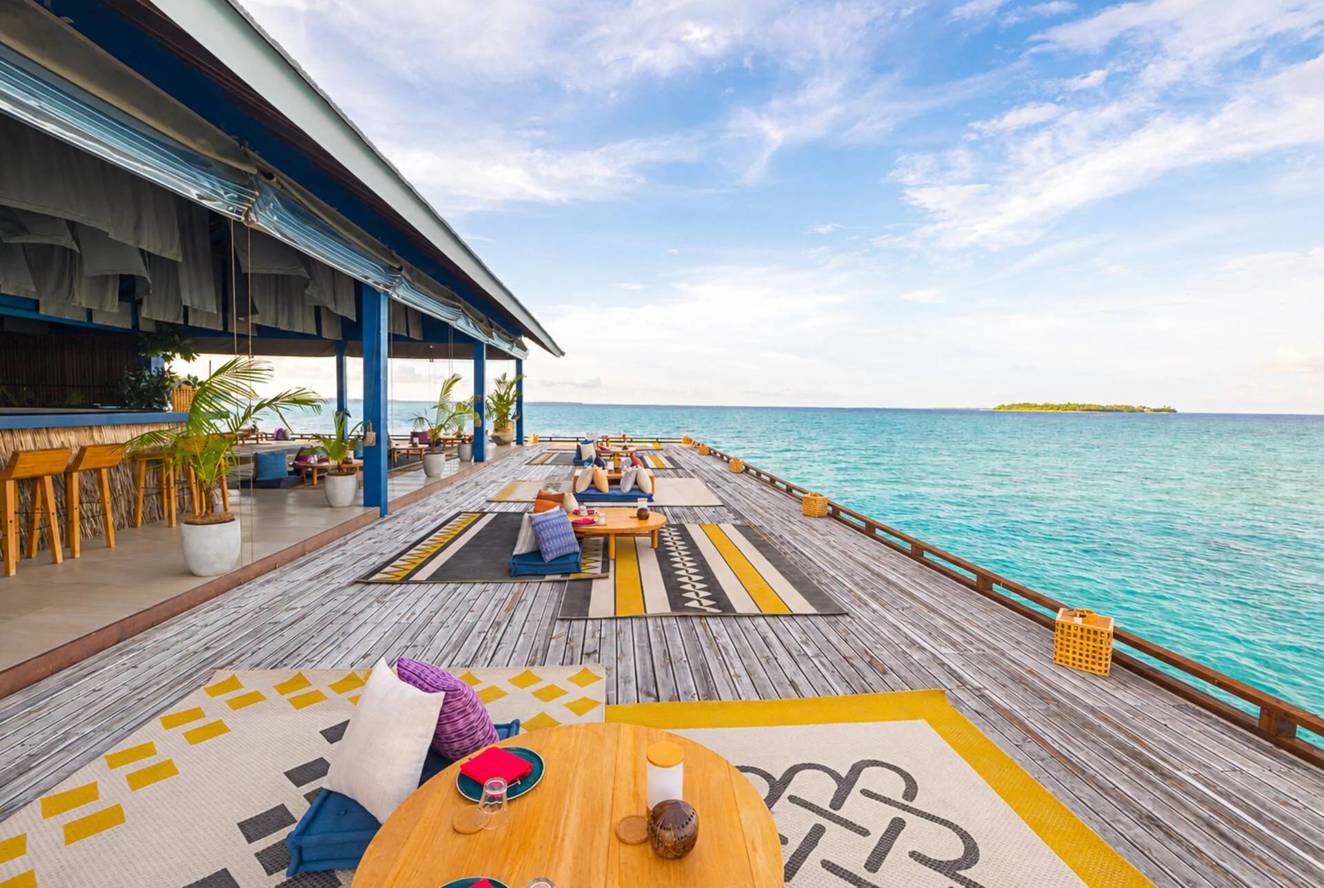 Guduguda's open-air overwater deck at The Standard, floor cushions and patterned rugs set along the boardwalk toward the lagoon