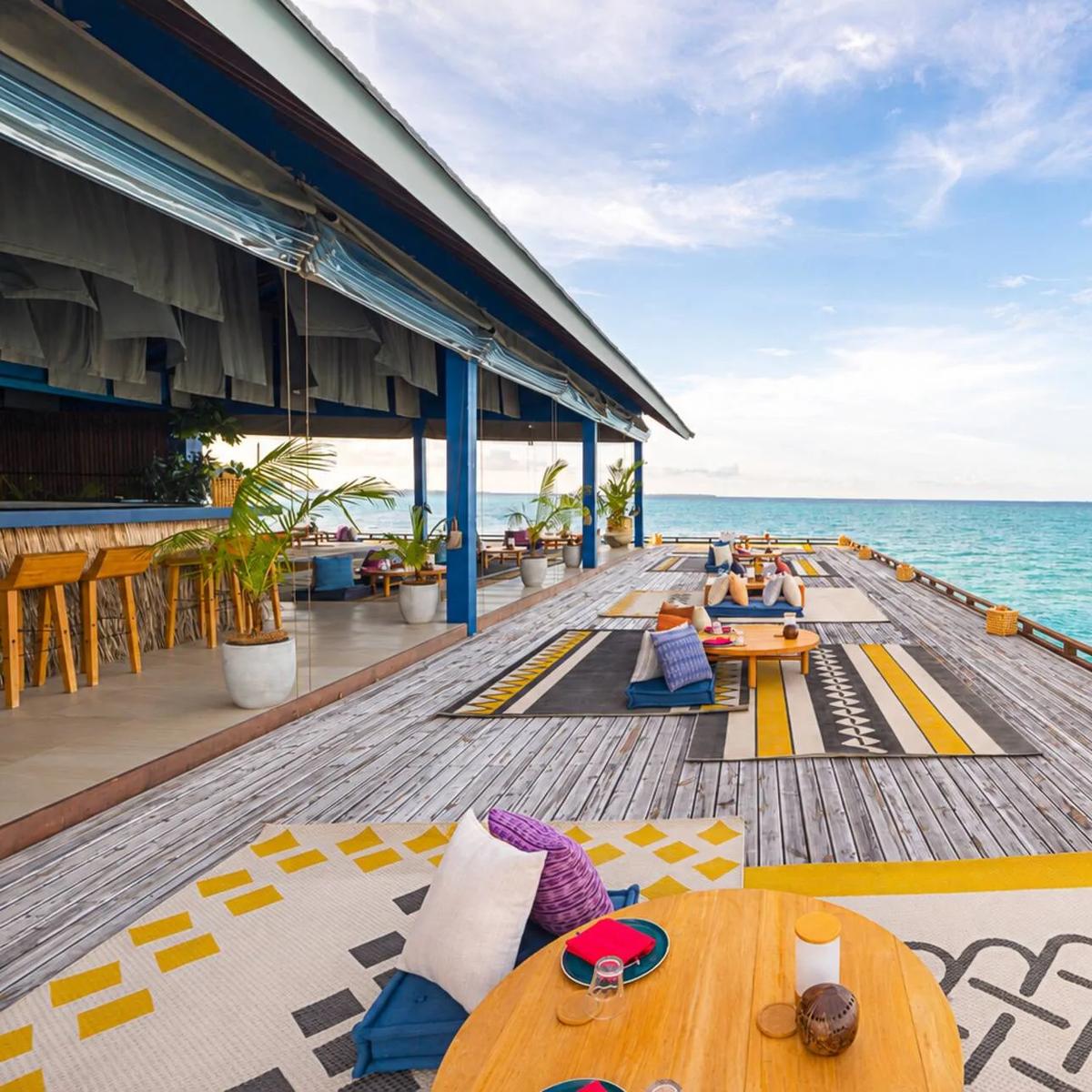 Guduguda's open-air overwater deck at The Standard, floor cushions and patterned rugs set along the boardwalk toward the lagoon