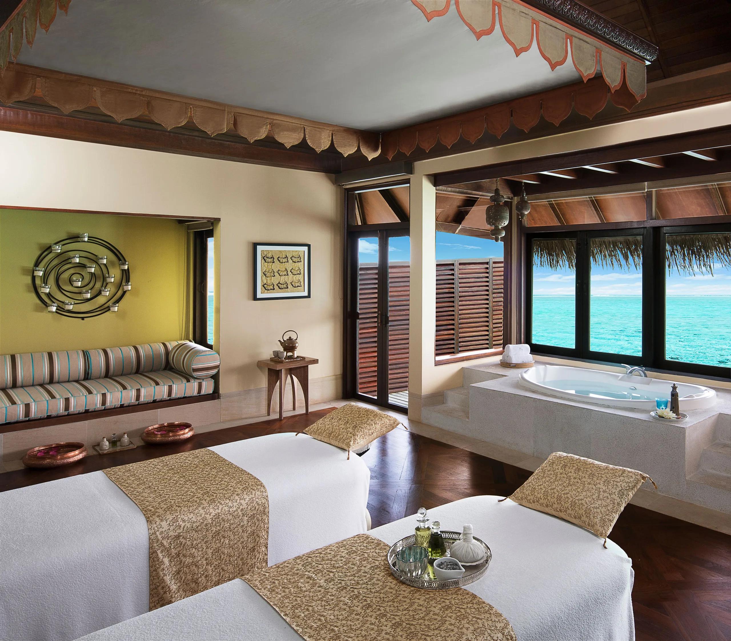 An overwater treatment suite with two massage beds and a jacuzzi tub looking out over the lagoon