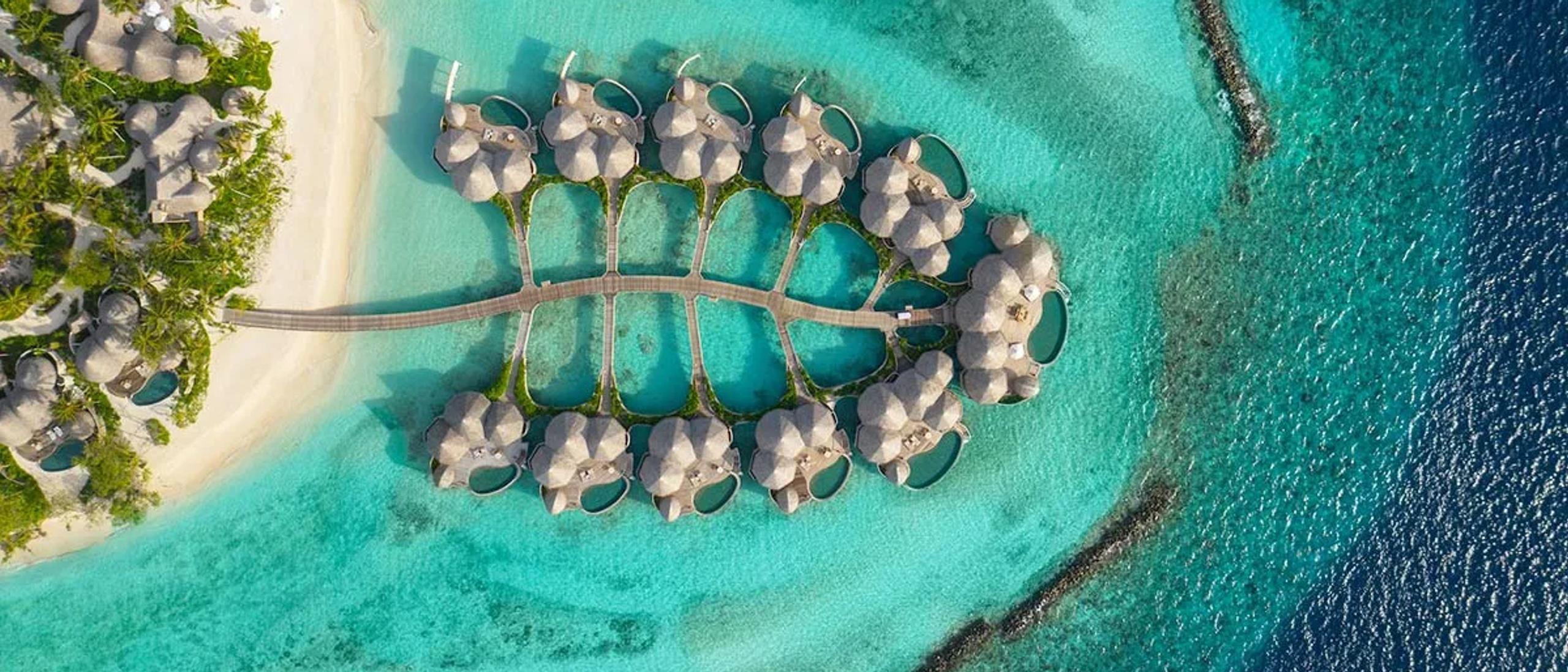 Aerial view of Nautilus Maldives' overwater Ocean Houses, arranged along a curved jetty over the Baa Atoll lagoon.
