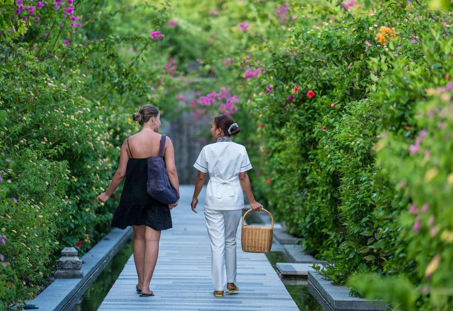 A guest is walked to treatment by a therapist along a flower-lined garden path at Essens Wellness and Spa