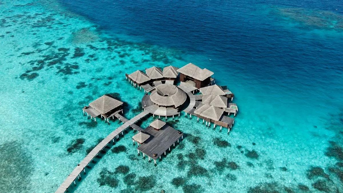 Aerial view of Coco Spa's overwater pavilions, connected by boardwalk, over the reef
