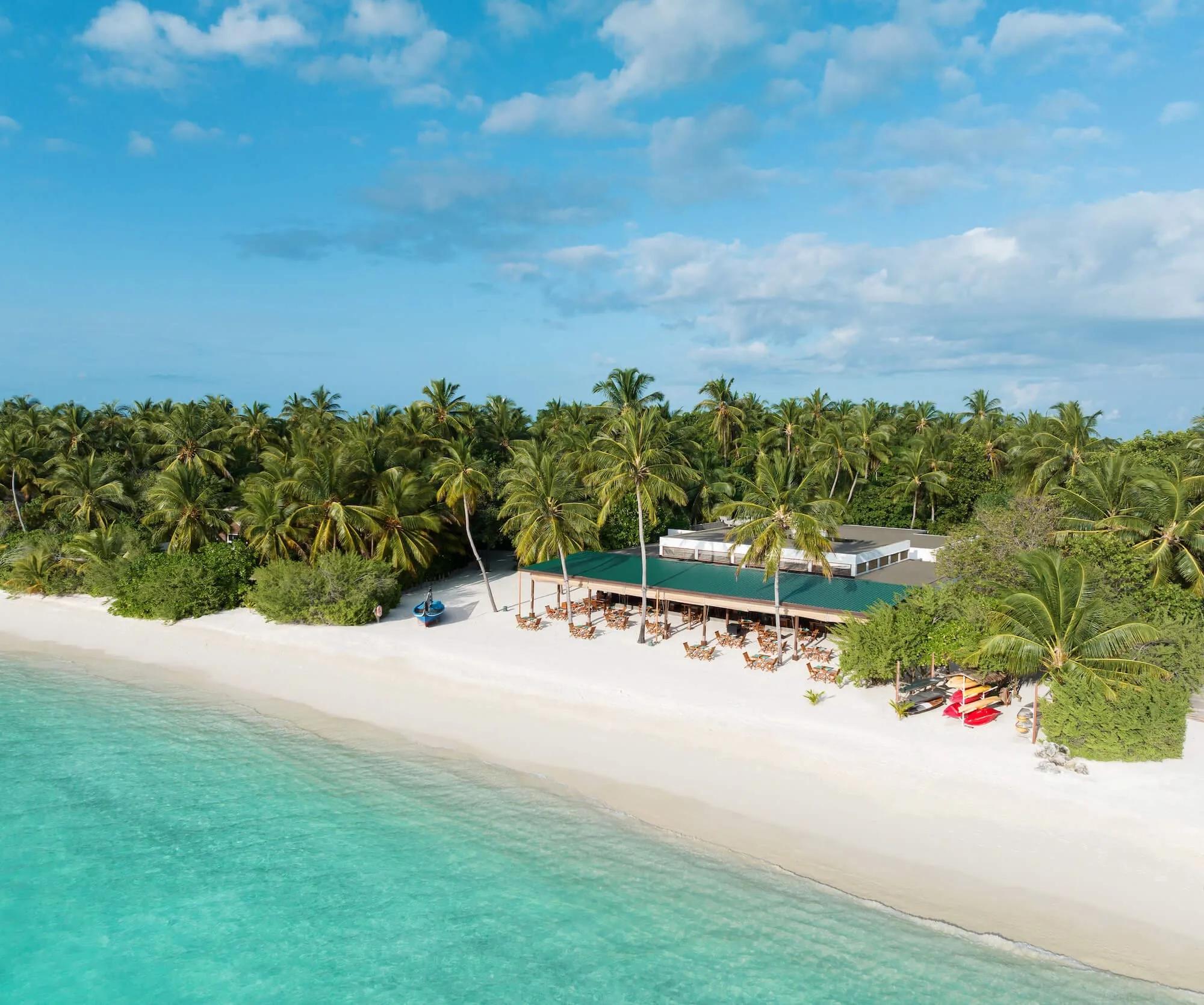 Aerial view of Raha Market's green-roofed dining pavilion on the beach, tables set beneath palm trees