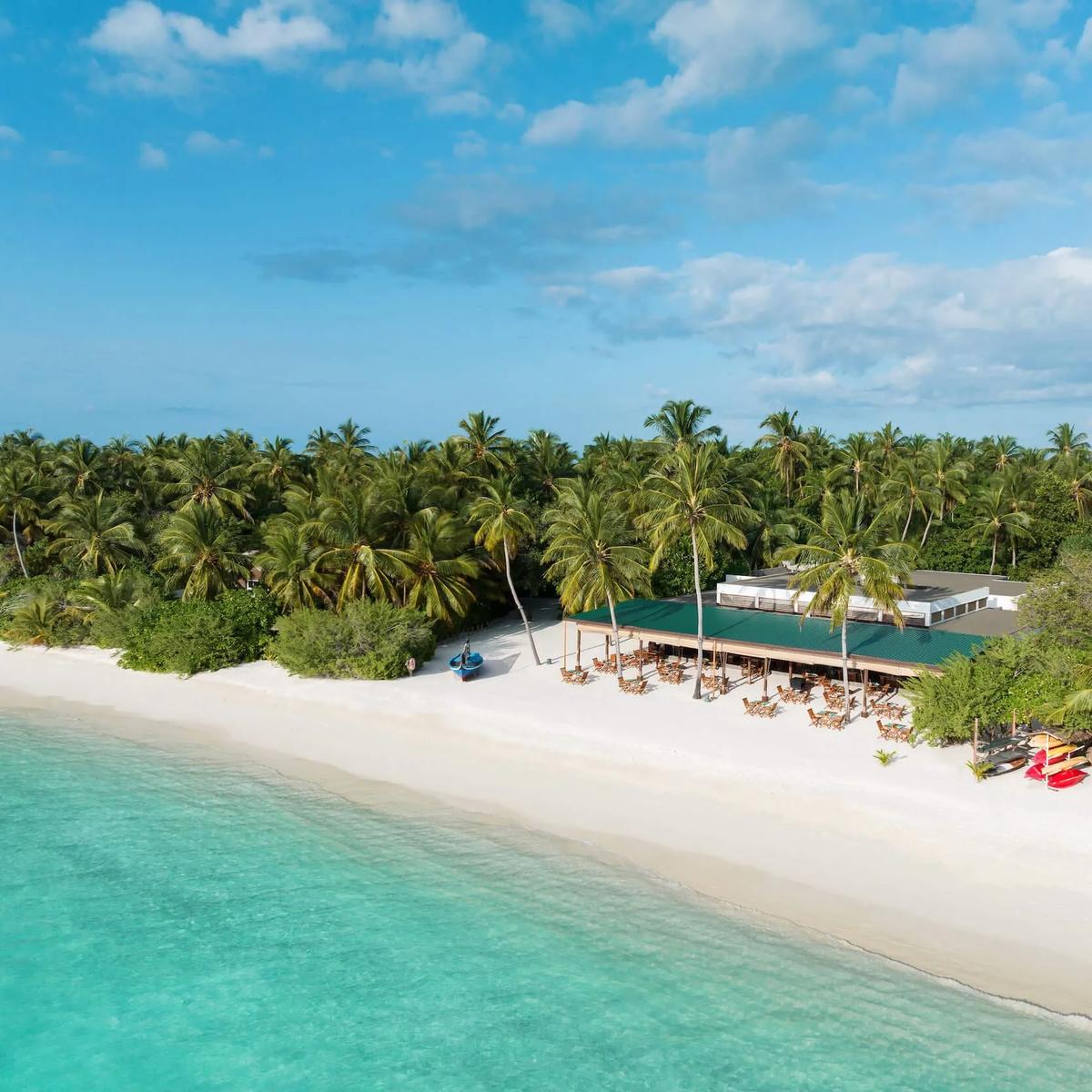 Aerial view of Raha Market's green-roofed dining pavilion on the beach, tables set beneath palm trees