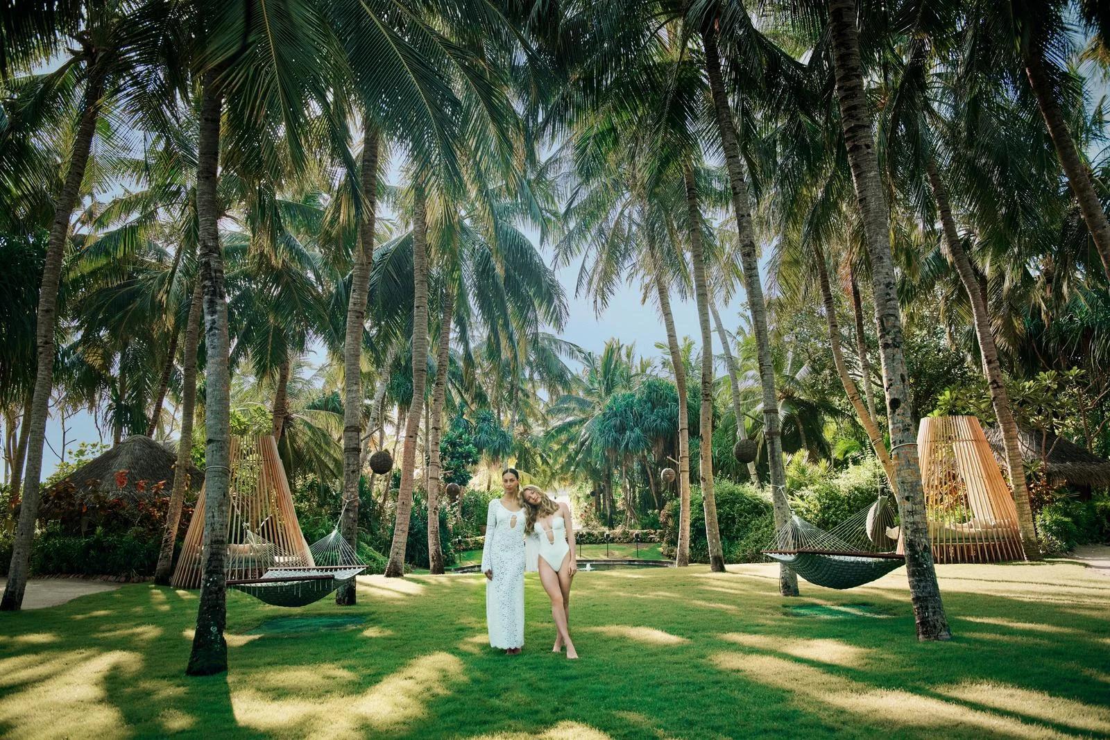 Two guests standing in the garden outside One&Only Spa, Reethi Rah, hammocks slung between the palm trees around them