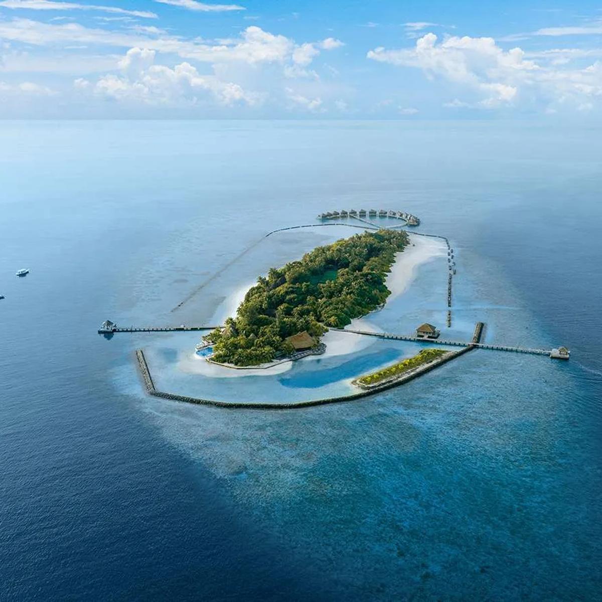 Aerial view of Komandoo's entire reef-ringed island, jetties reaching out to overwater villas on the northern tip and boats crossing the lagoon
