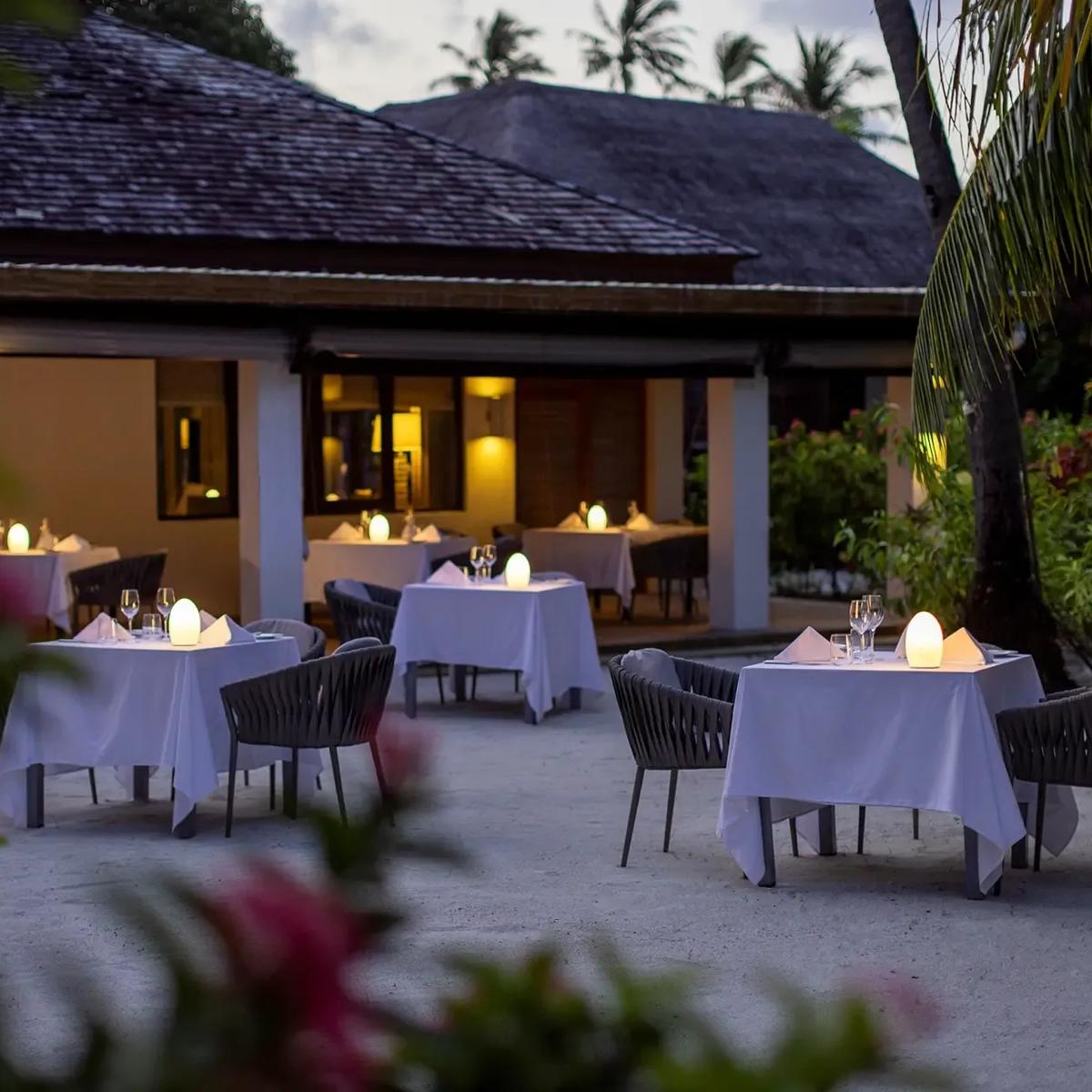 Candlelit tables set for dinner on Etesian's garden terrace at dusk