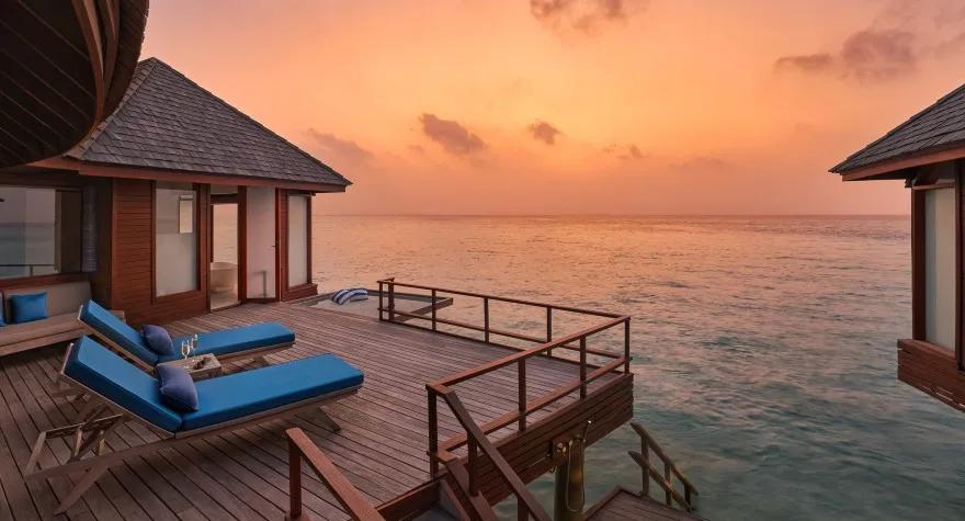 The private deck of a Sunset Over Water Suite at dusk, loungers set above the lagoon