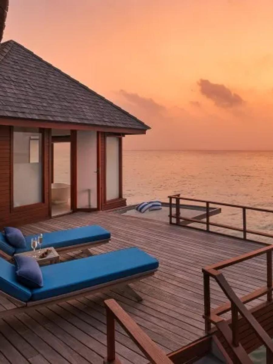The private deck of a Sunset Over Water Suite at dusk, loungers set above the lagoon