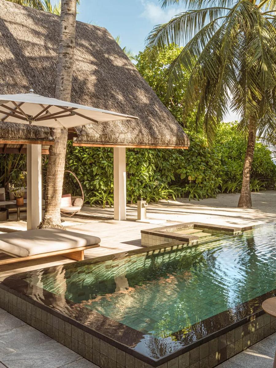 A Family Beach Villa's pool deck set under palm trees, with a thatched pavilion and the beach visible beyond