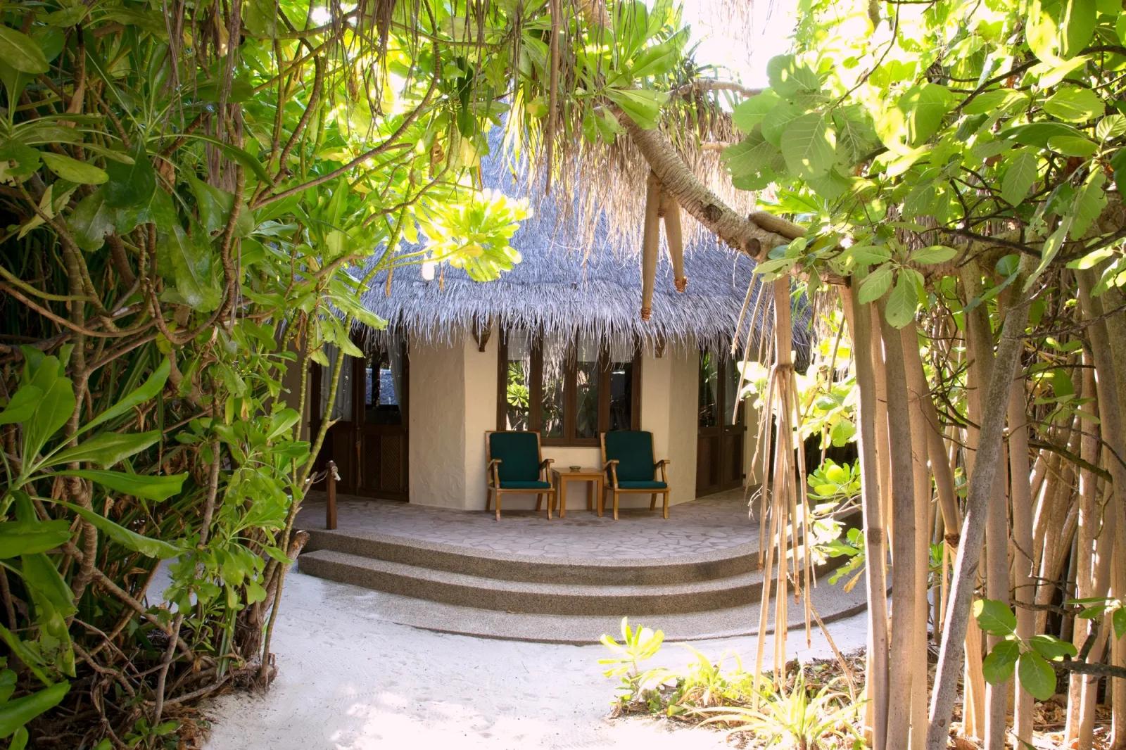 A thatched-roof villa glimpsed through jungle foliage on the sandy path from the beach