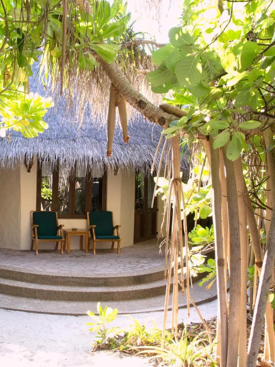 A thatched-roof villa glimpsed through jungle foliage on the sandy path from the beach