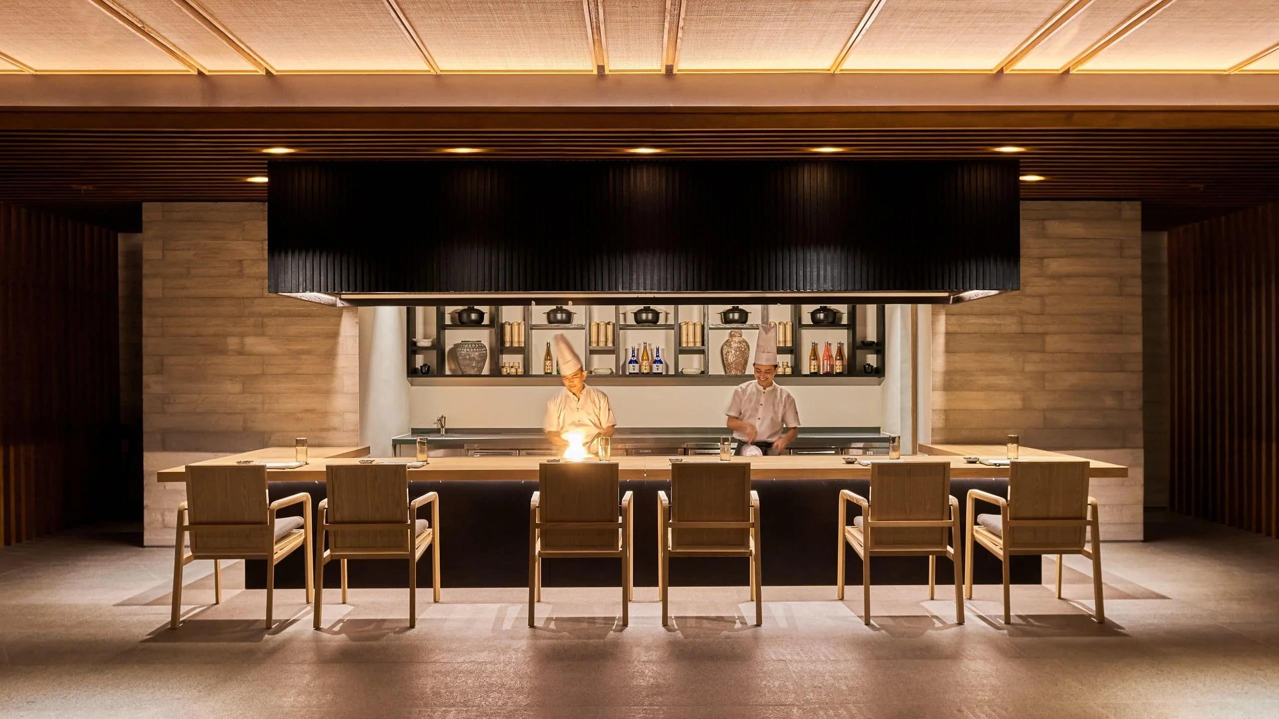 A chef sends flame up from the teppanyaki grill at Umami, guests seated around the counter