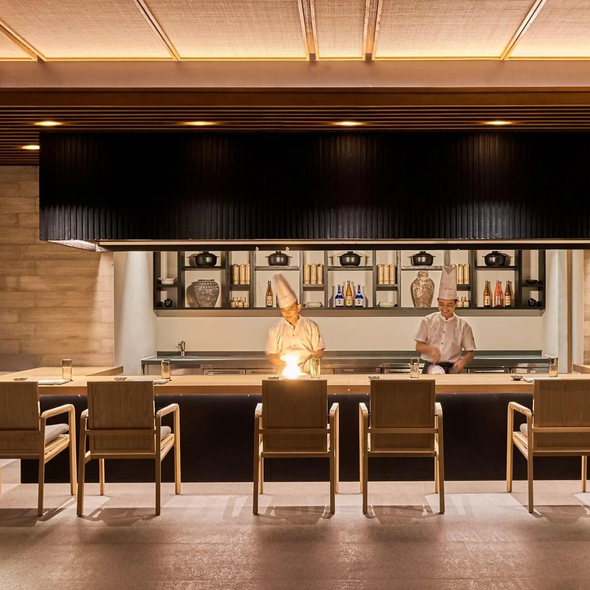 A chef sends flame up from the teppanyaki grill at Umami, guests seated around the counter