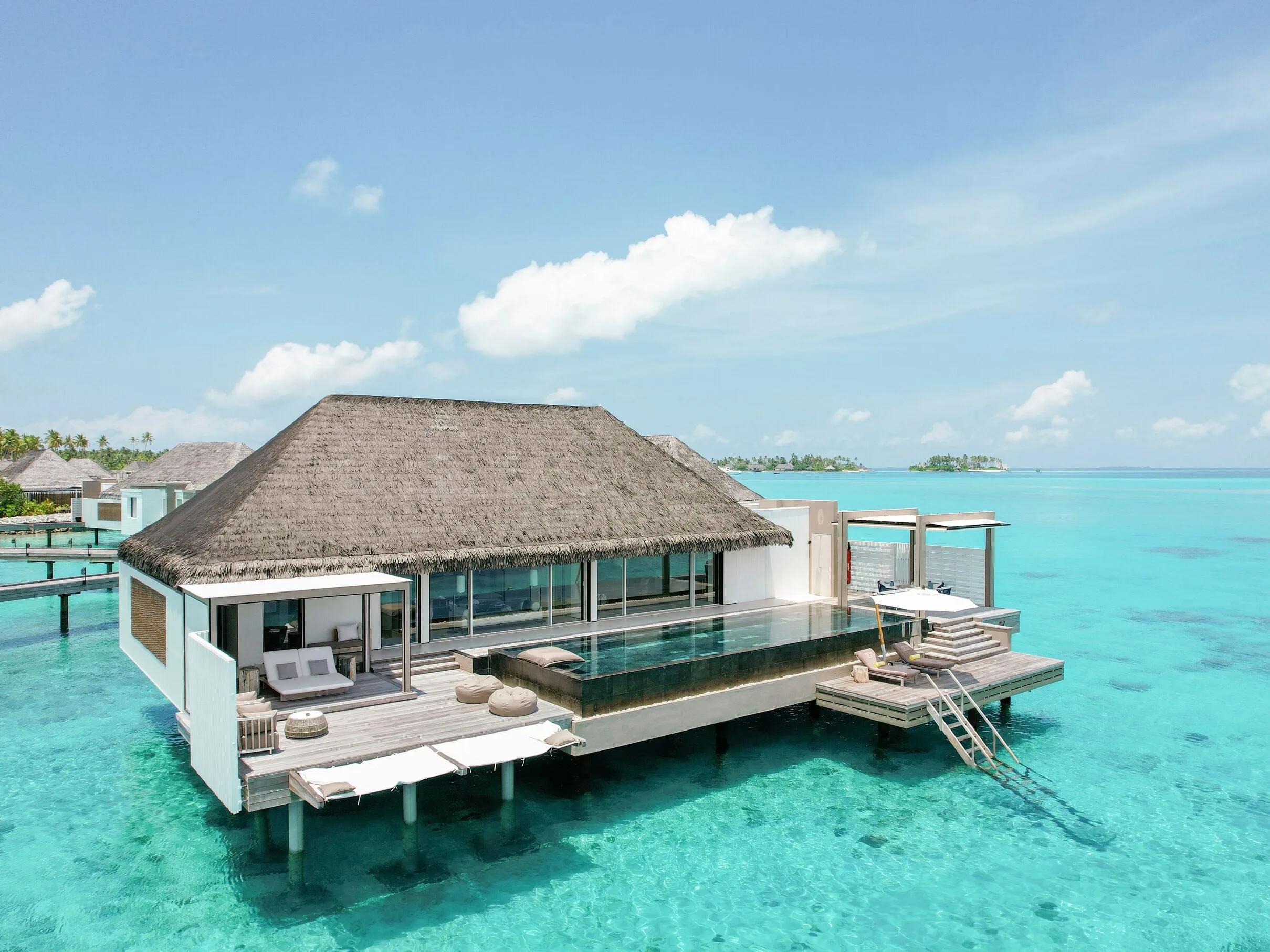 The Horizon Villa's infinity pool extending toward the open lagoon, thatched pavilion and daybeds on the deck