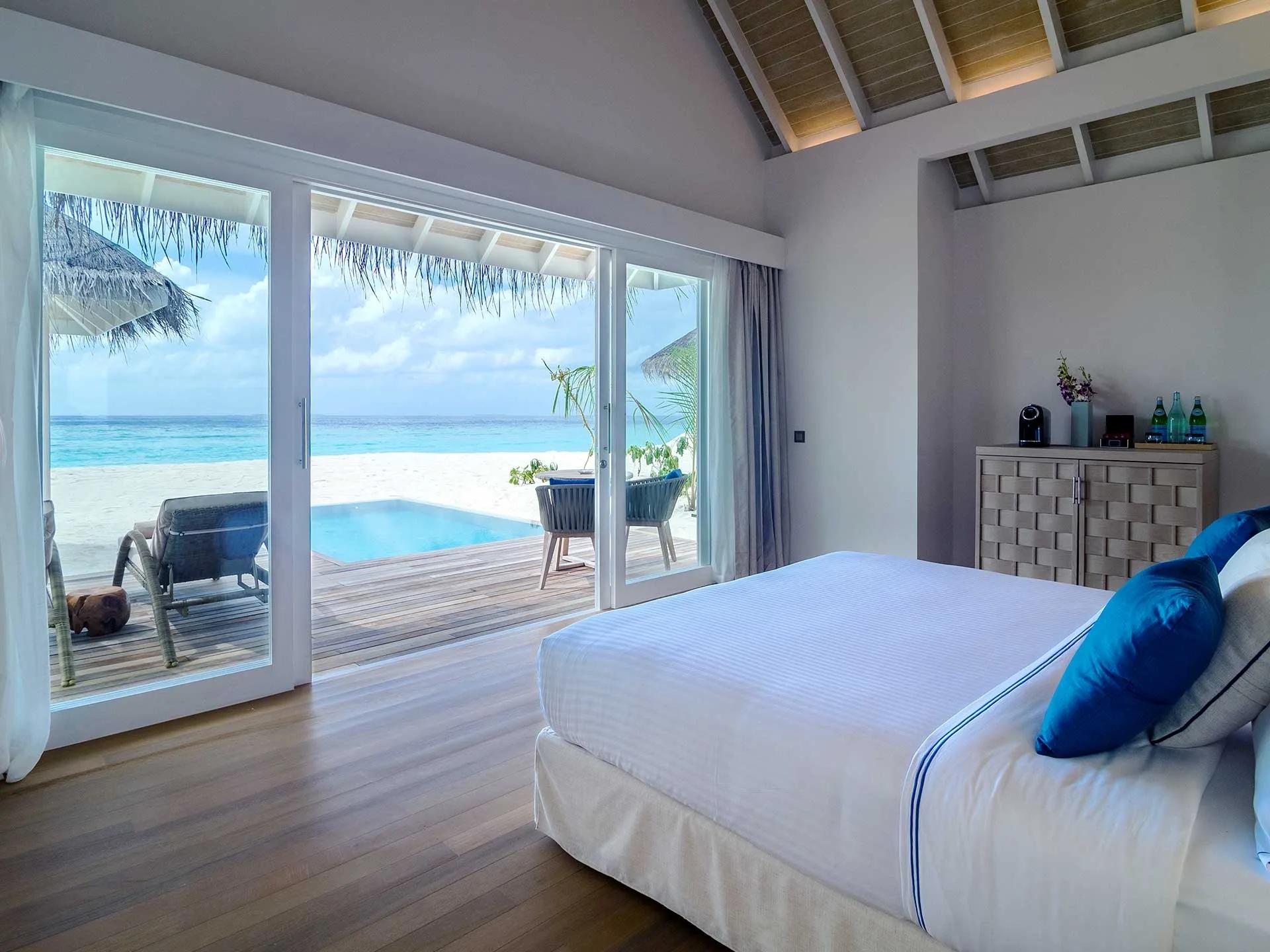 A Deluxe Beach Villa with Pool's bedroom opening onto its private plunge pool and sun loungers, with the open lagoon beyond