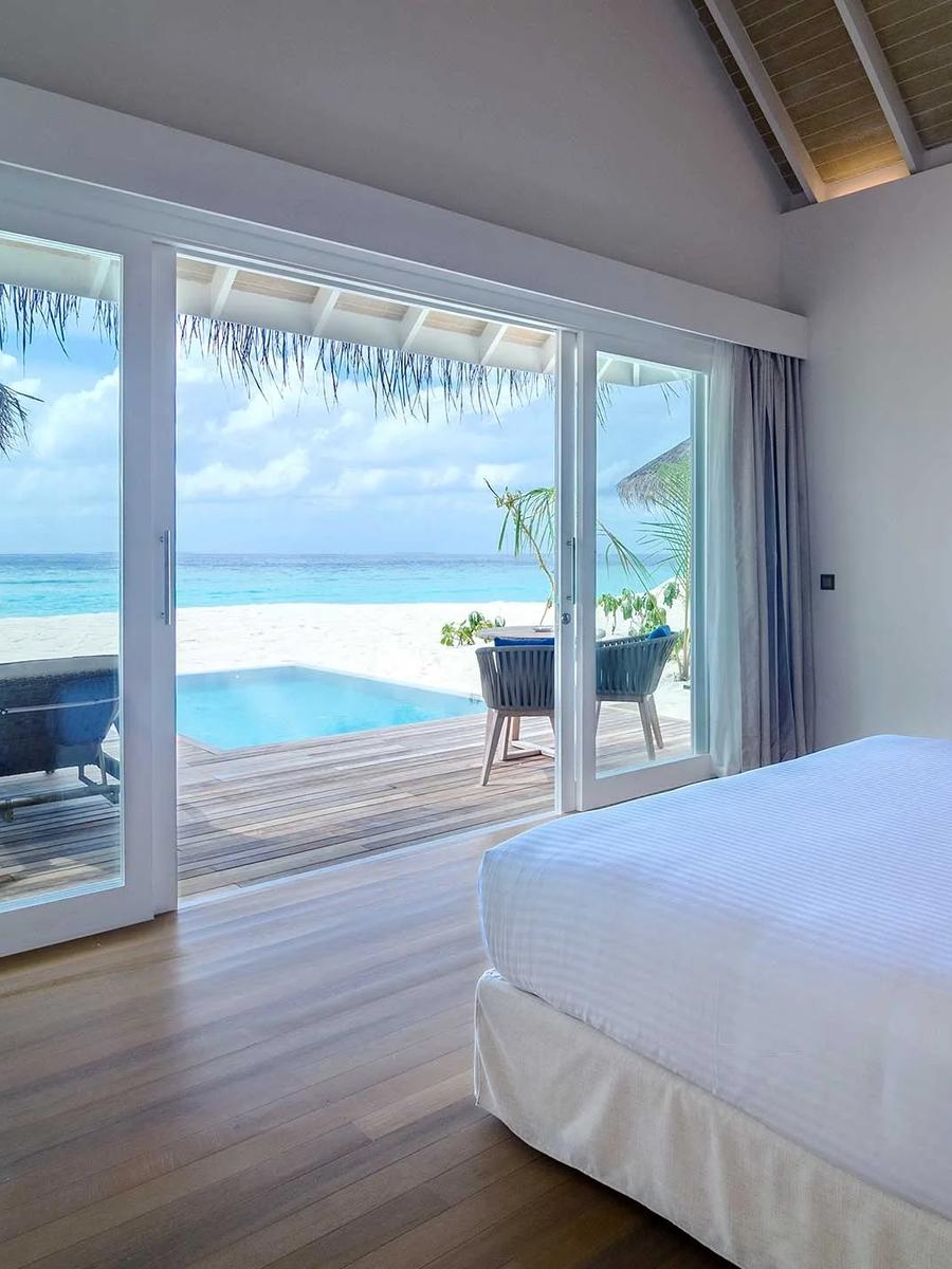 A Deluxe Beach Villa with Pool's bedroom opening onto its private plunge pool and sun loungers, with the open lagoon beyond
