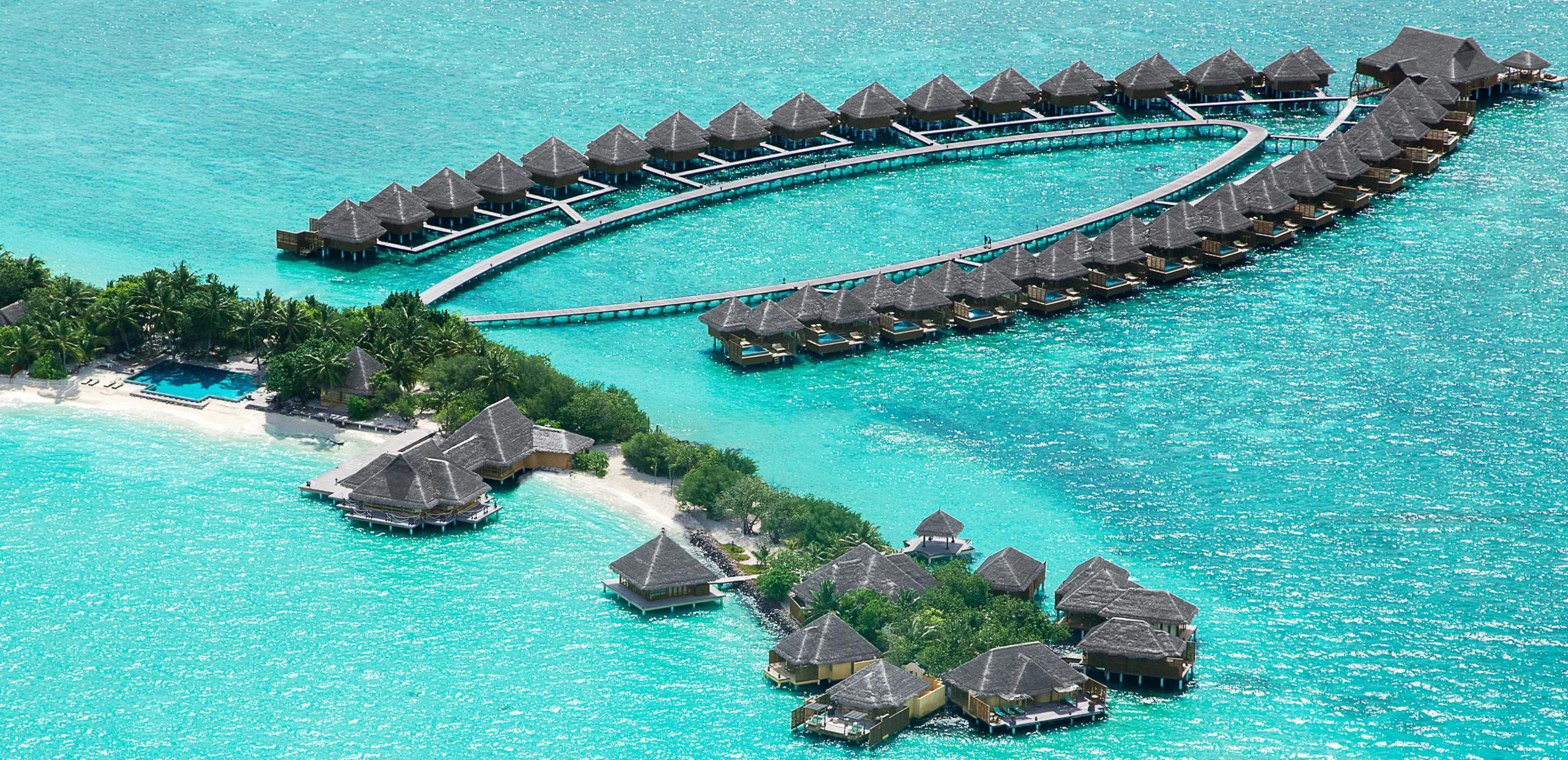 An aerial view of Taj Exotica's overwater villas curving out into the lagoon from Emboodhu Finolhu, with the beach and main pool in the foreground