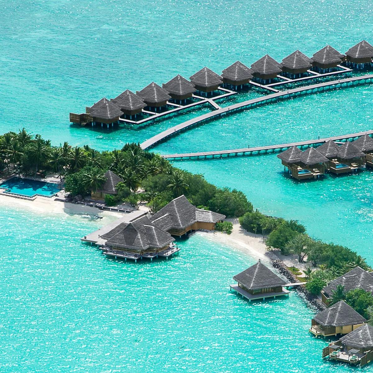 An aerial view of Taj Exotica's overwater villas curving out into the lagoon from Emboodhu Finolhu, with the beach and main pool in the foreground
