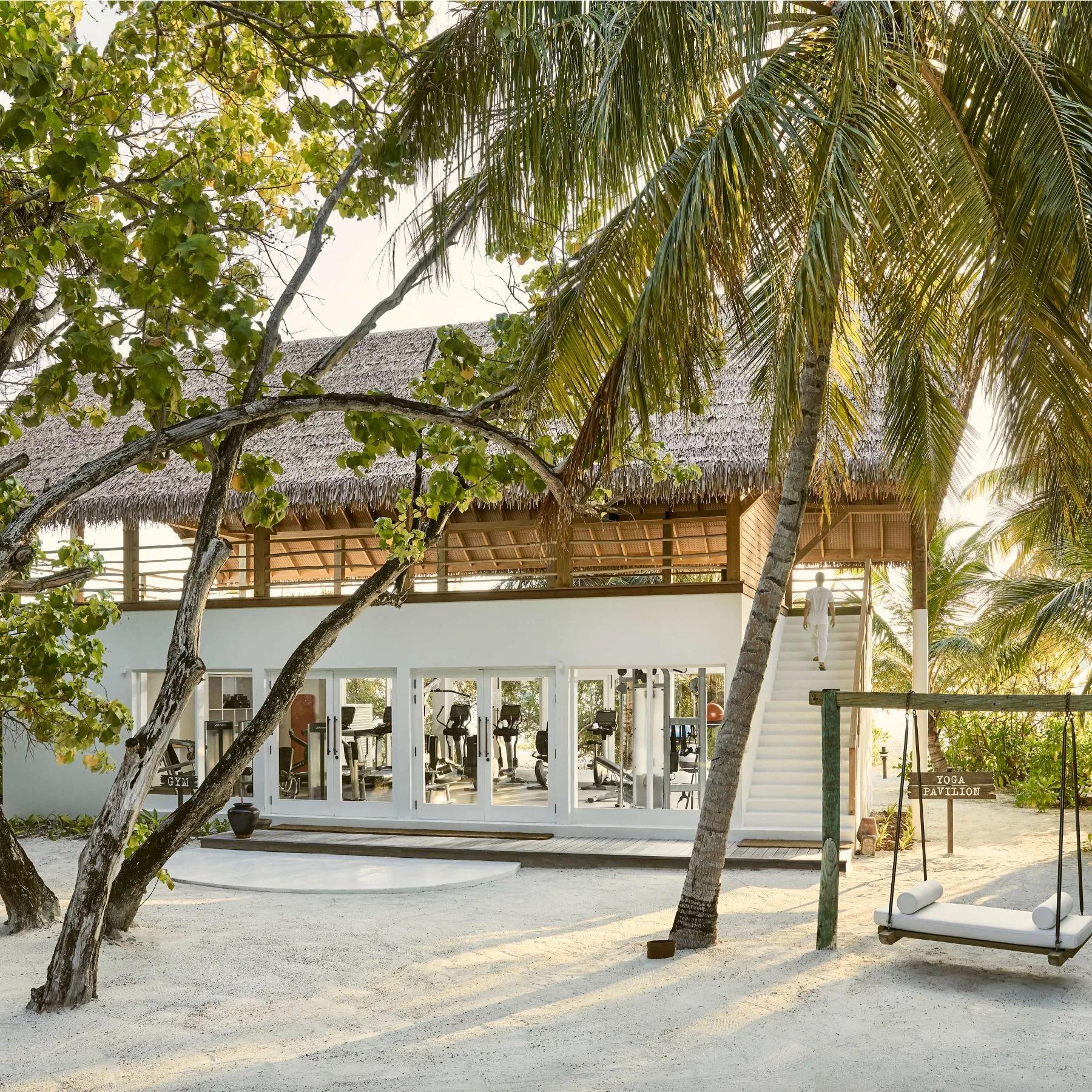 The gym and yoga pavilion building among the palm trees, with a beach swing in the foreground