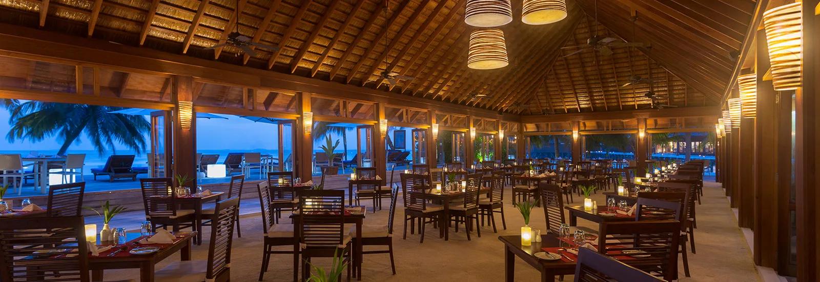 Ahima Restaurant's open-air dining room at dusk, tables set beside the beach