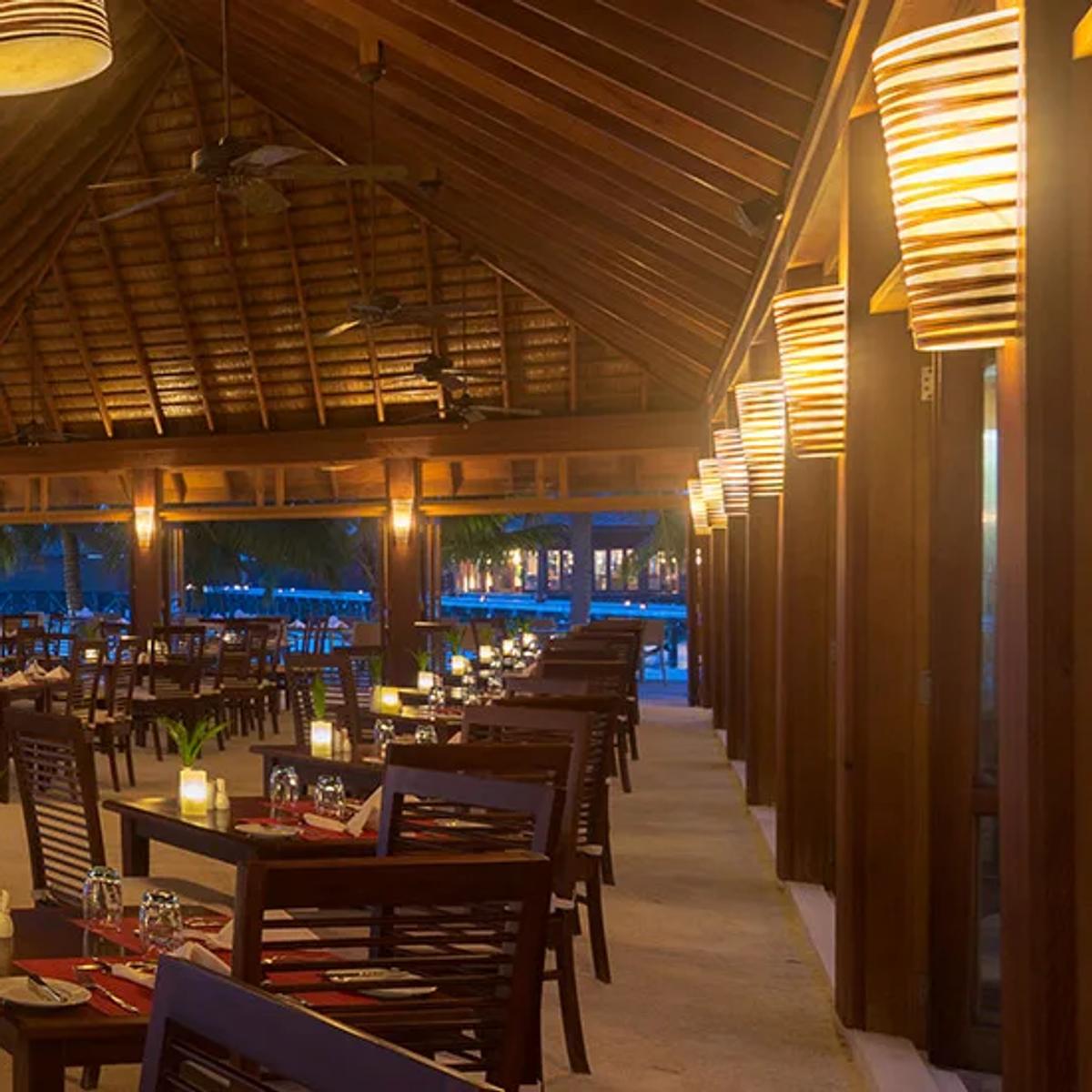 Ahima Restaurant's open-air dining room at dusk, tables set beside the beach