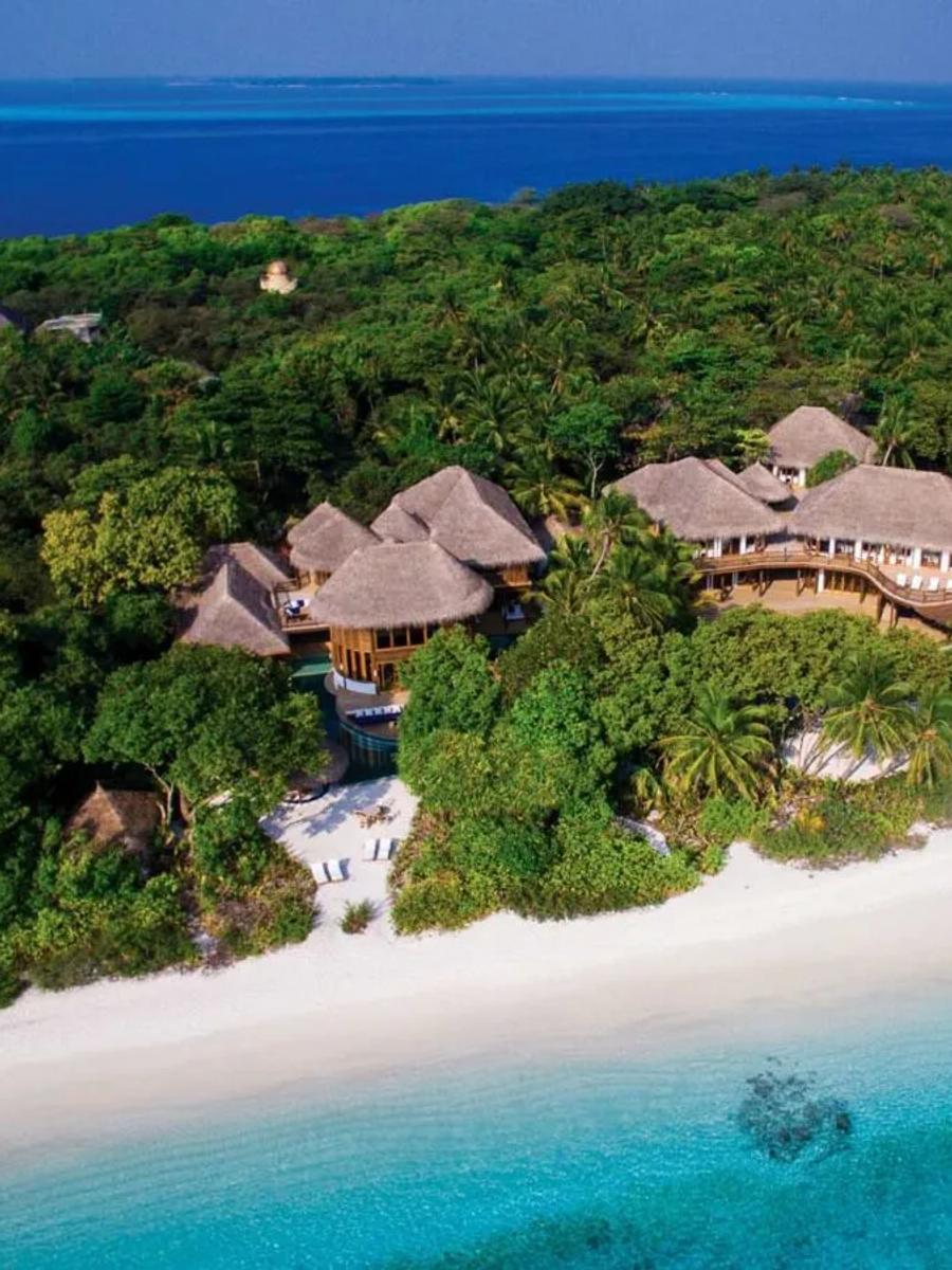 An aerial view of a beachfront three-bedroom villa complex — thatched roofs and a private pool set among jungle, steps from the beach and the reef beyond