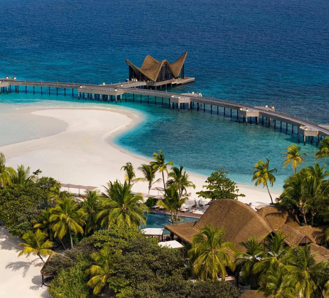 JOALI's overwater dining pavilion at the end of the jetty, its wing-shaped thatched roof over the lagoon, with a white sandbank alongside