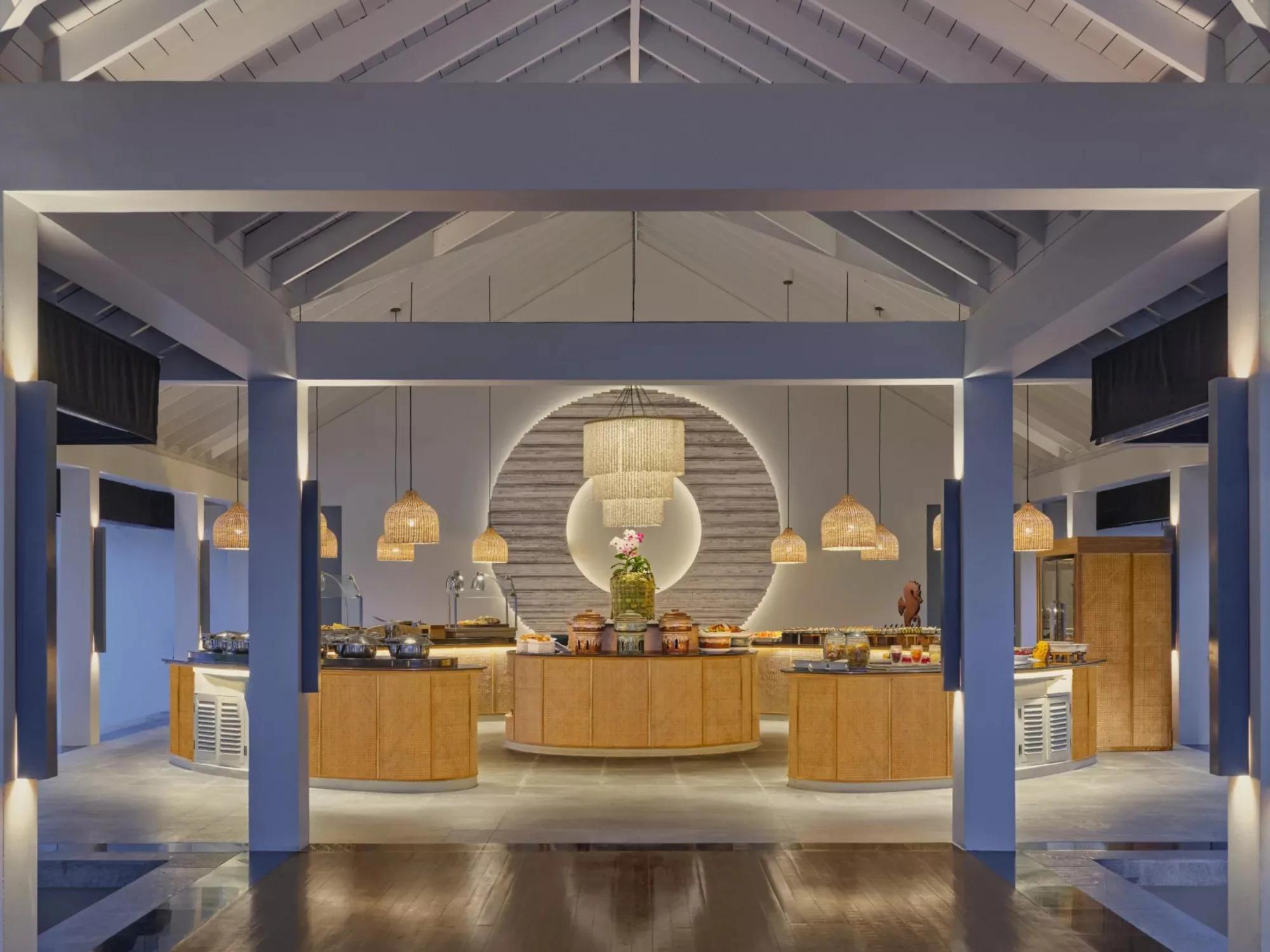 Palms Restaurant's buffet counters at Noku Maldives, lit beneath woven pendant lamps