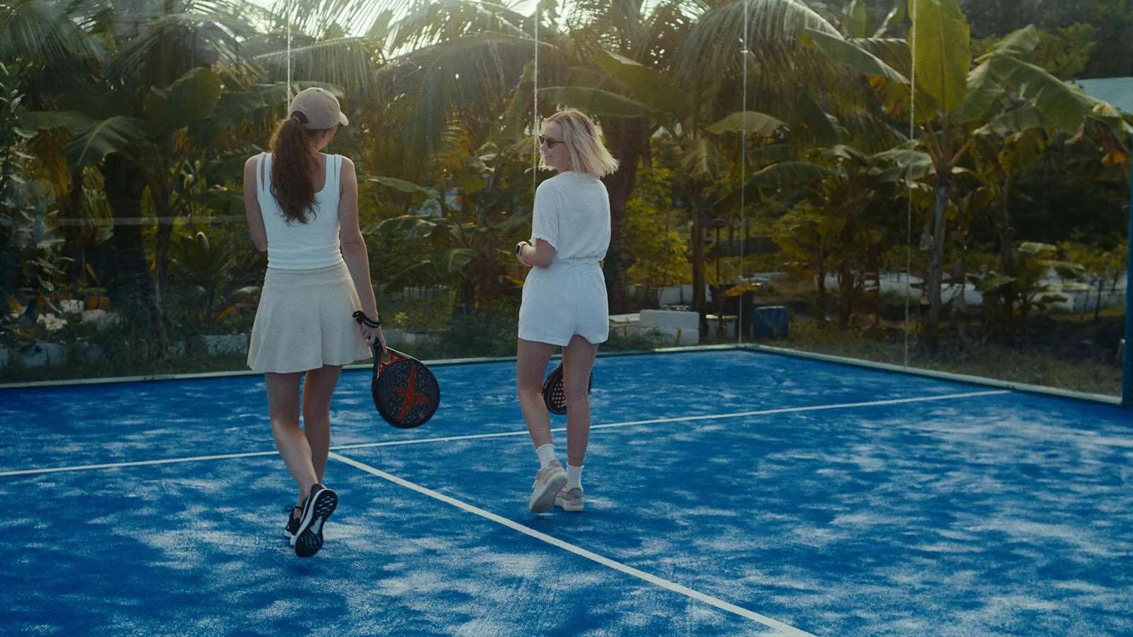 Two guests walking off the Panoramic Padel Tennis Court, rackets in hand, palm trees behind