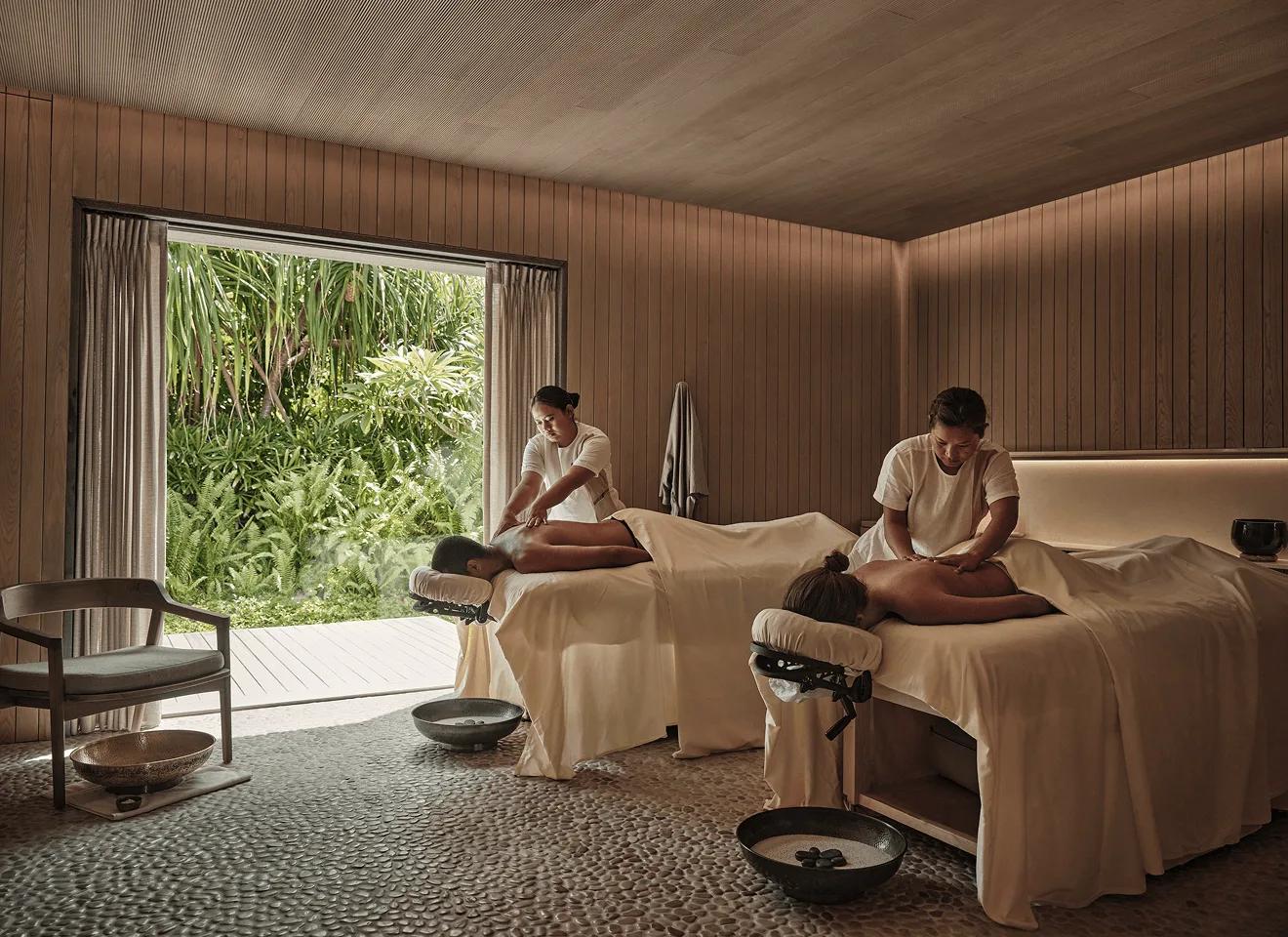 Two guests receiving a treatment side by side in a wood-panelled room at FLOW, garden visible through the open doorway