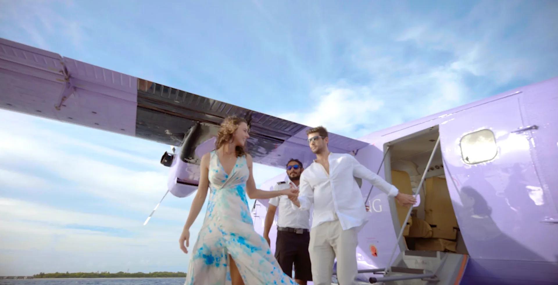 A couple stepping down from a purple Nautilus Maldives seaplane, met by the pilot on the pontoon.