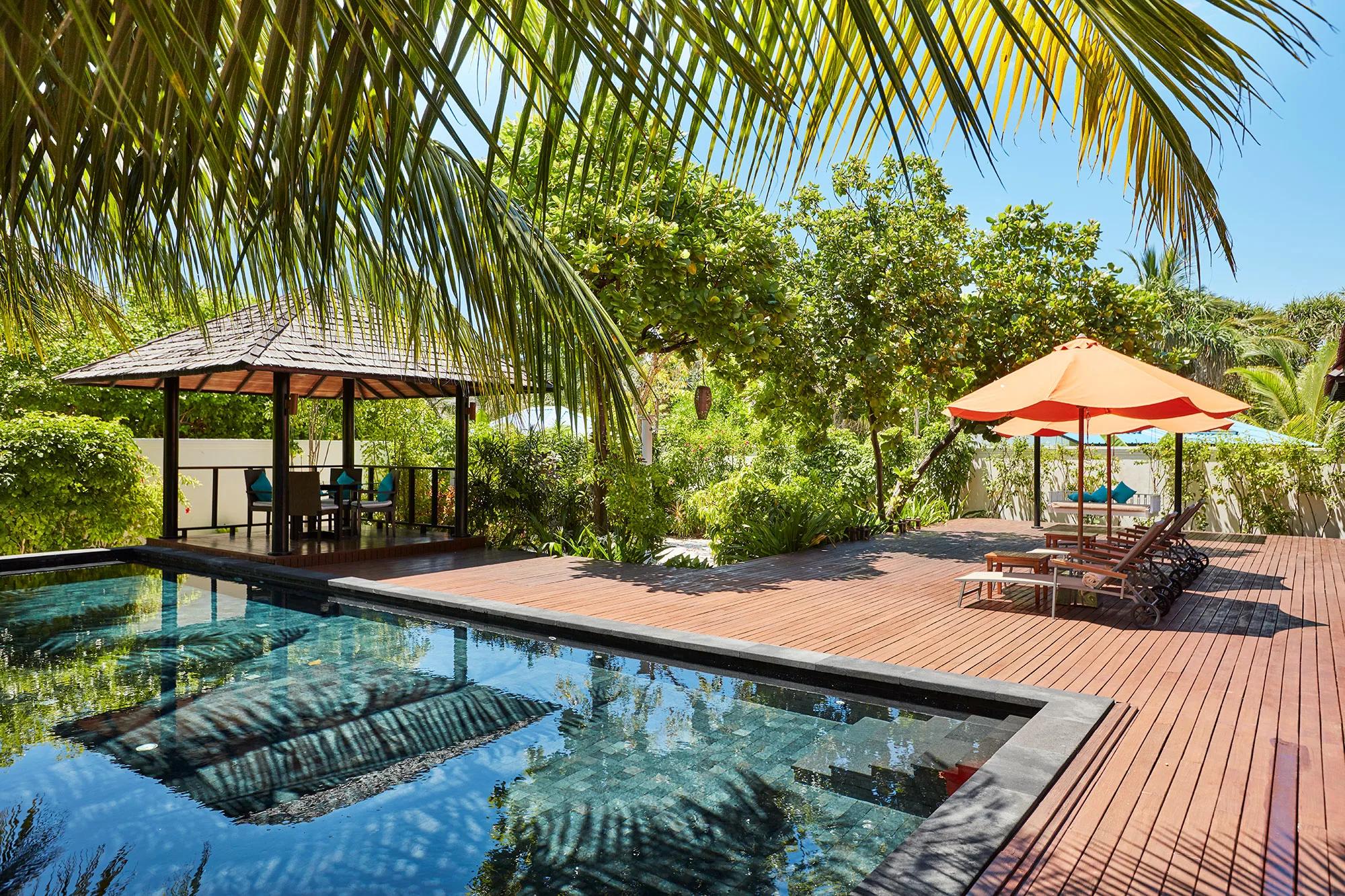 A private plunge pool beside a thatched garden pavilion at a Hidden Retreat villa, orange-cushioned loungers under palm cover