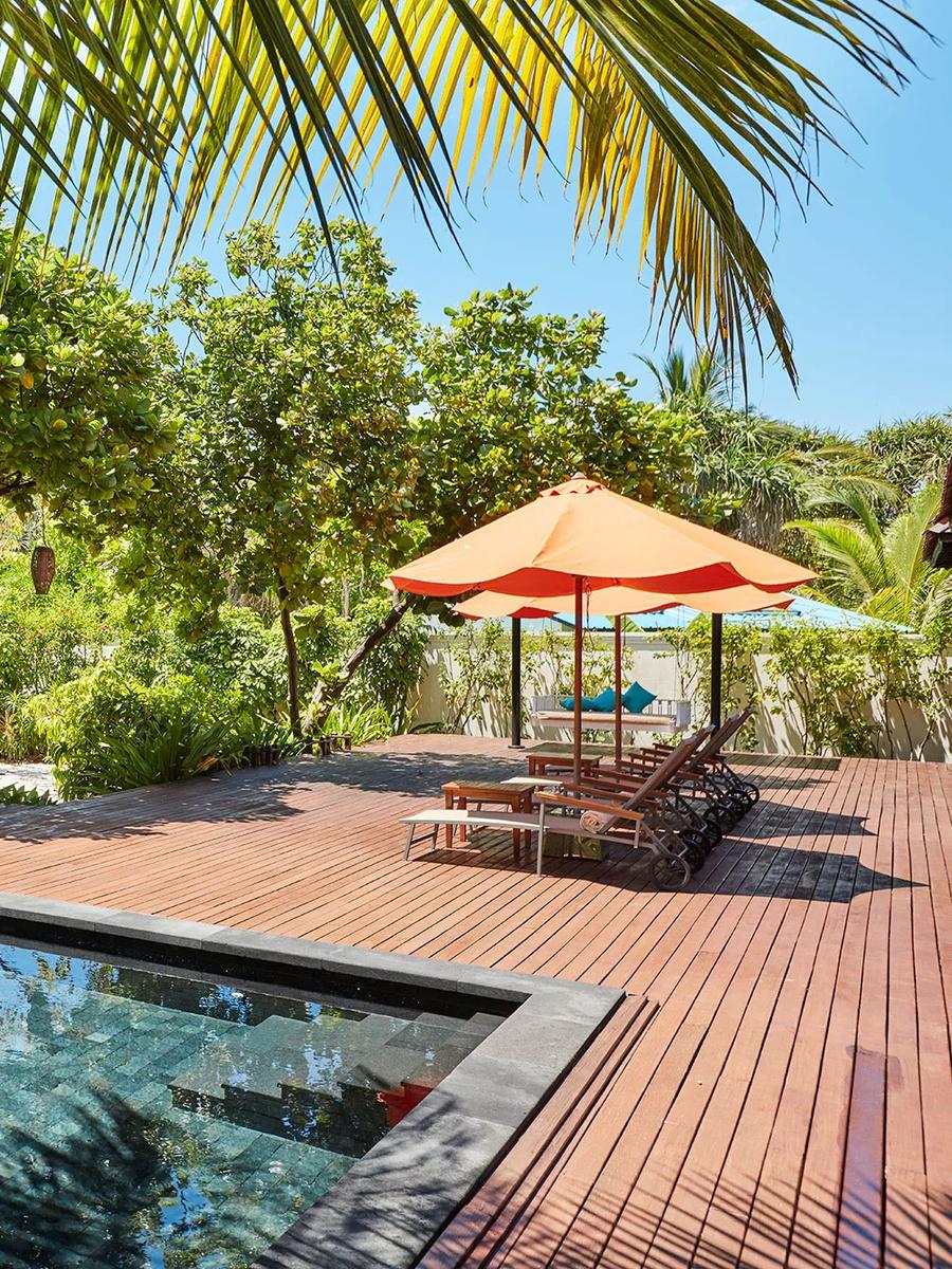 A private plunge pool beside a thatched garden pavilion at a Hidden Retreat villa, orange-cushioned loungers under palm cover