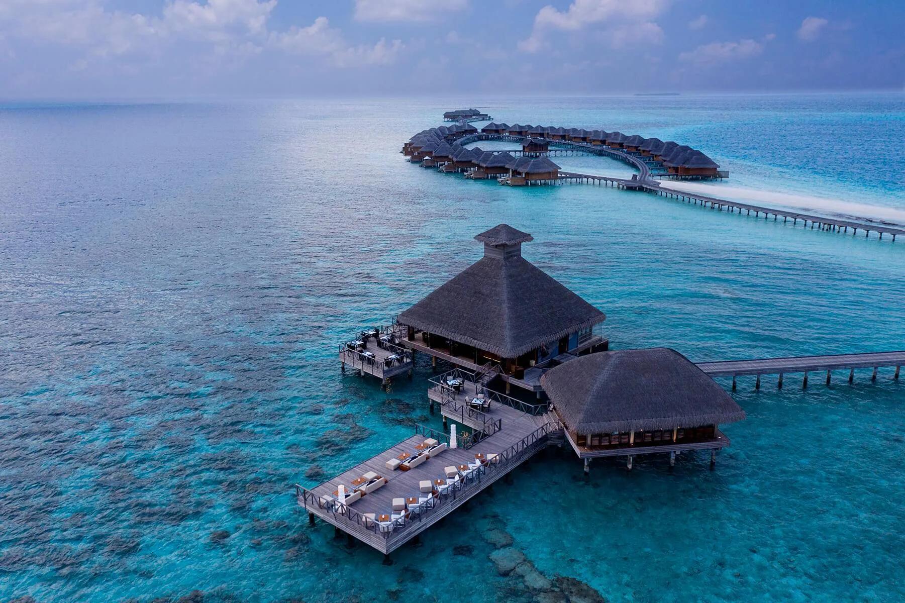 Salt's overwater thatched-roof dining pavilion at dusk, connected by jetty to the resort's row of villas